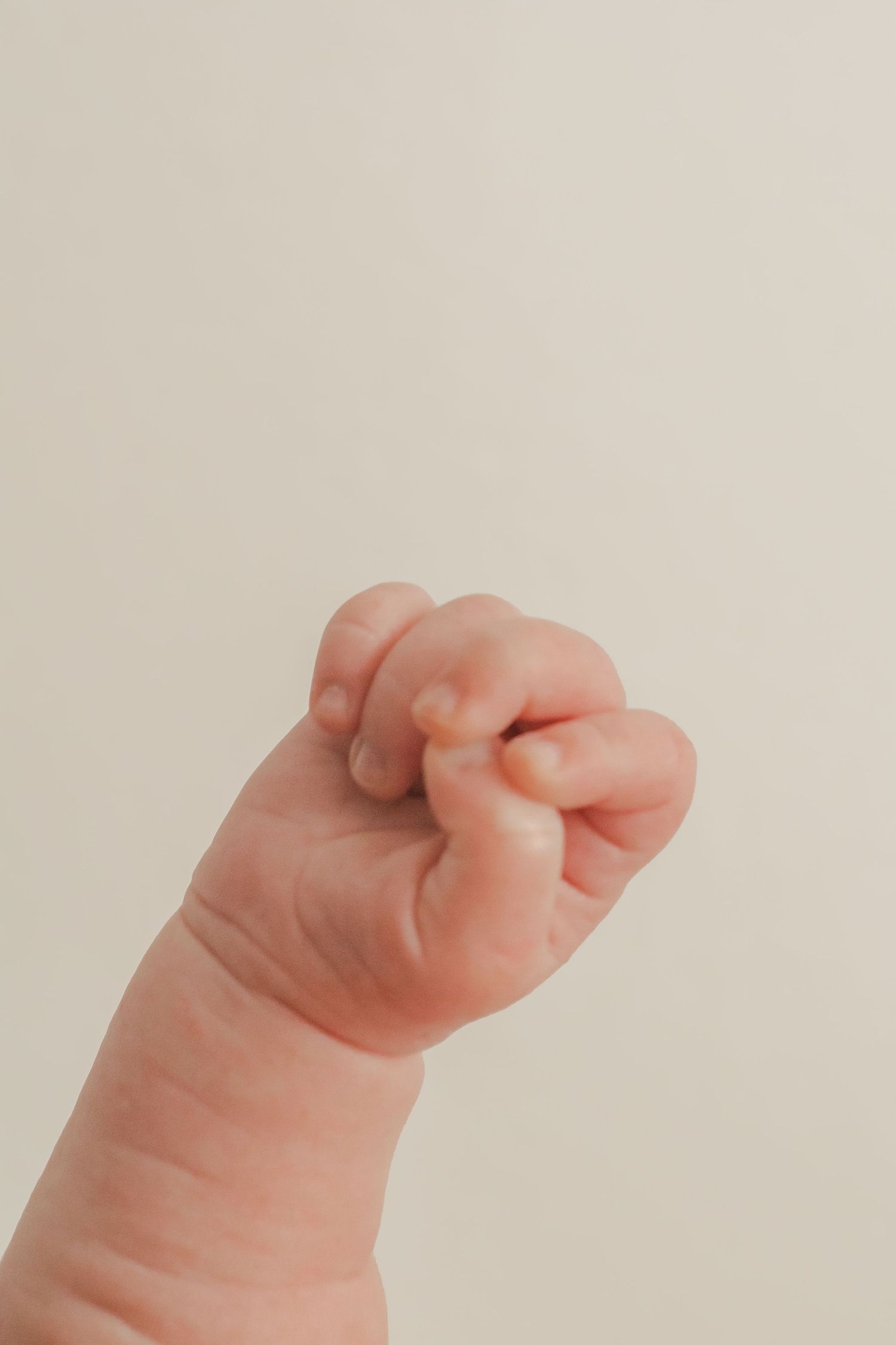 Close-up of a tiny newborn baby's fist against a light beige background.