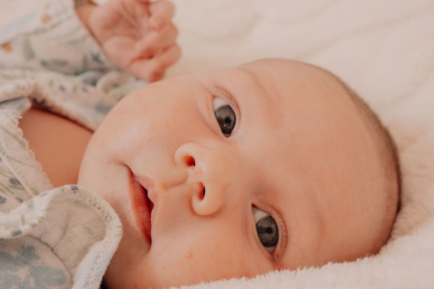 A newborn baby lies on soft fabric while gazing directly at the camera with bright eyes.