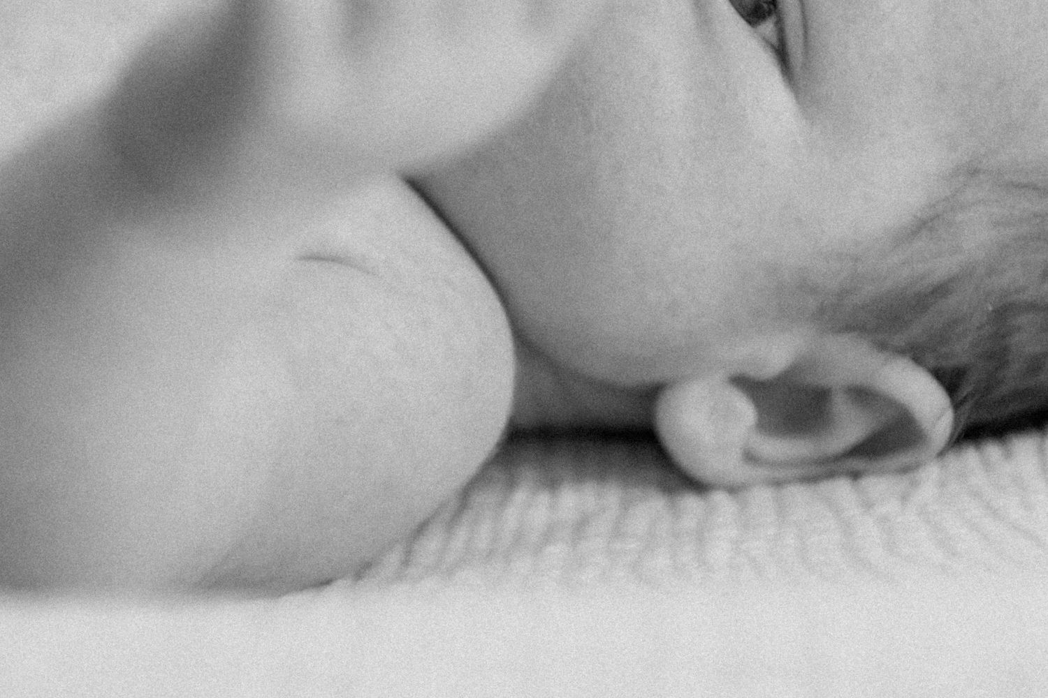 Black and white close-up photo of a tiny baby ear and cheek resting on white bedding.
