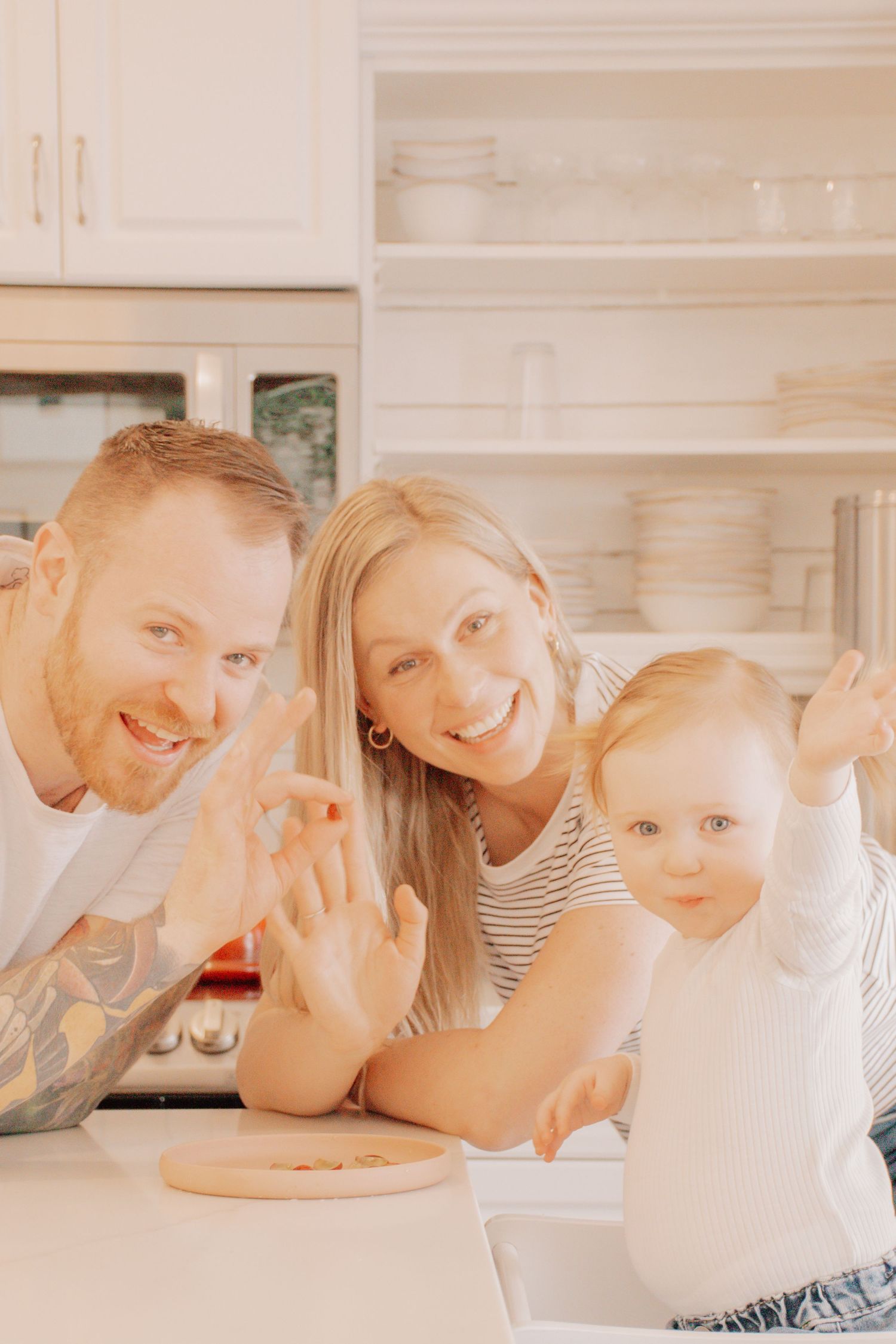 Three people smile together around a kitchen counter in warm lighting.