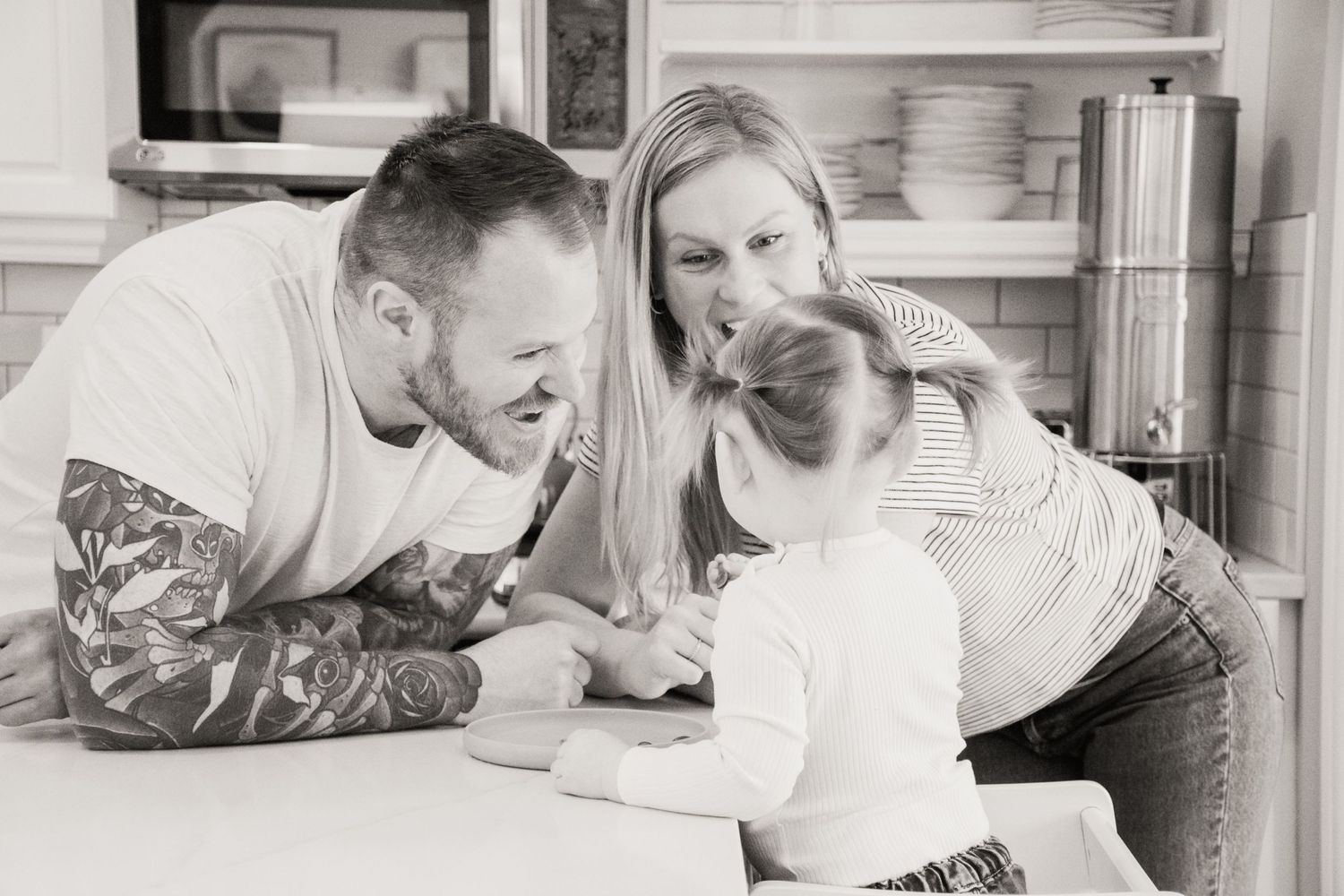 Two people laugh together while looking at a smartphone screen on a kitchen counter in black and white photo.