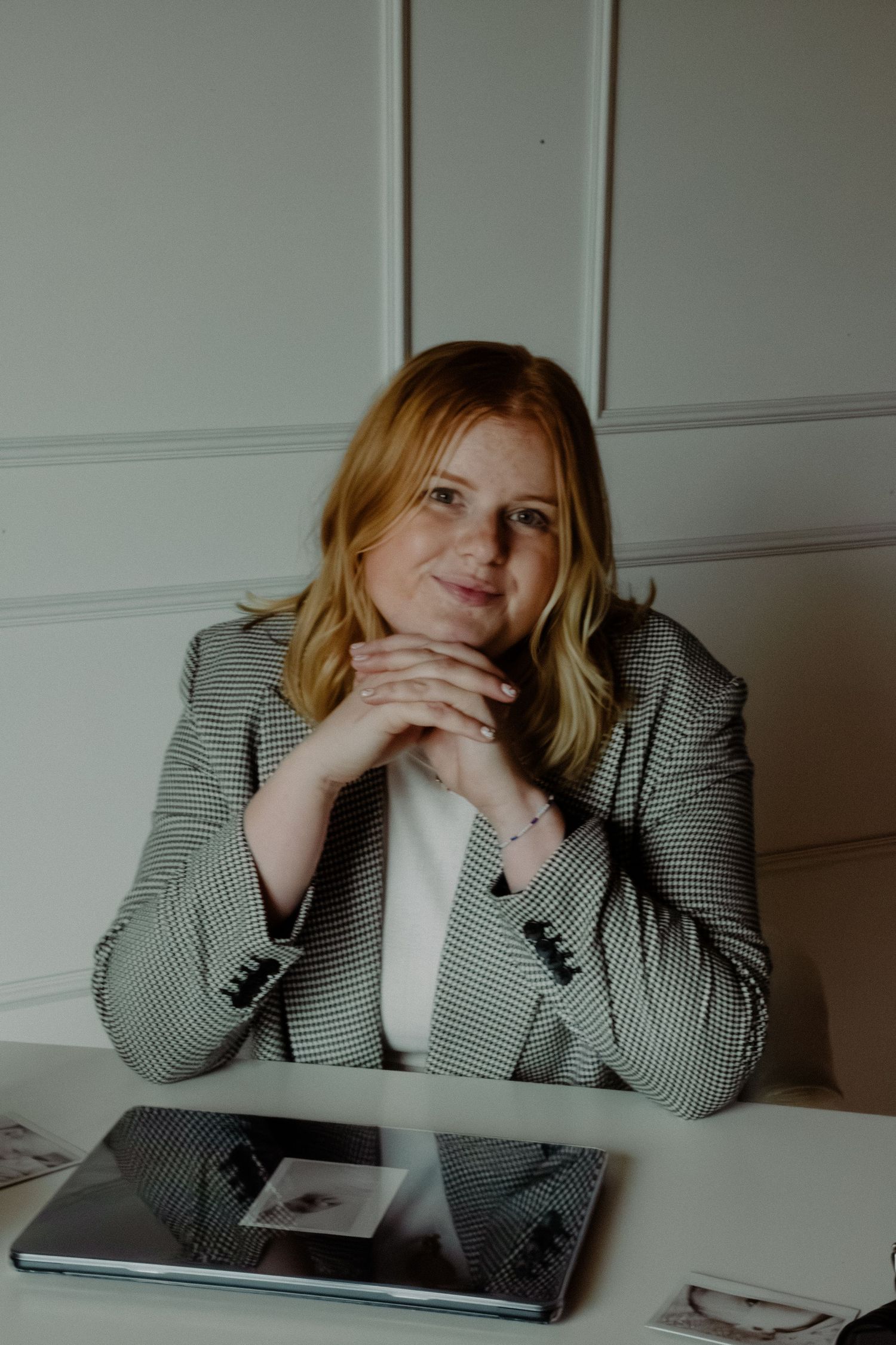 Person in black and white checkered blazer rests head on hand while sitting at desk with digital tablet.