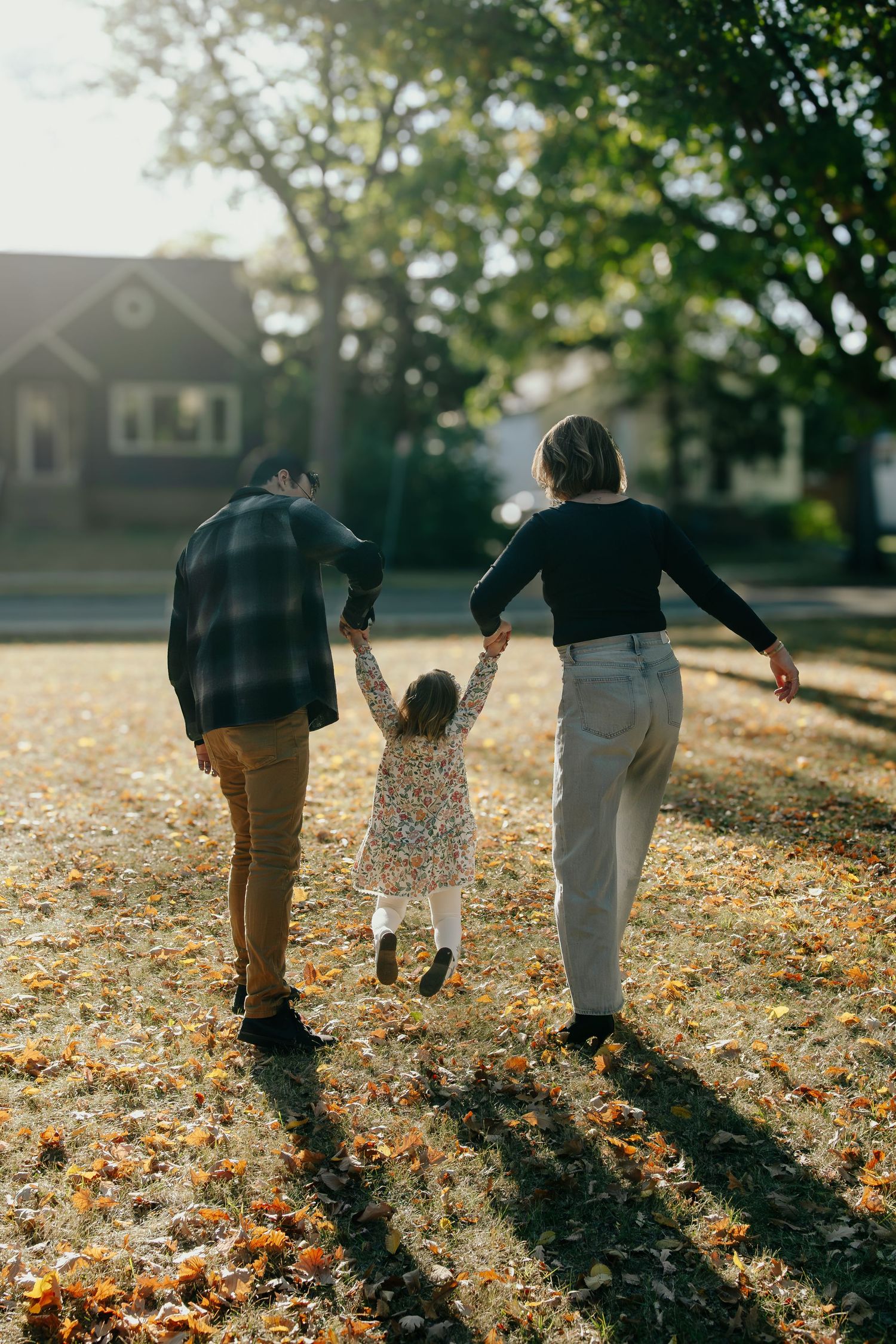 A family walks together holding hands on an autumn day with fallen leaves and long shadows cast by golden sunlight.