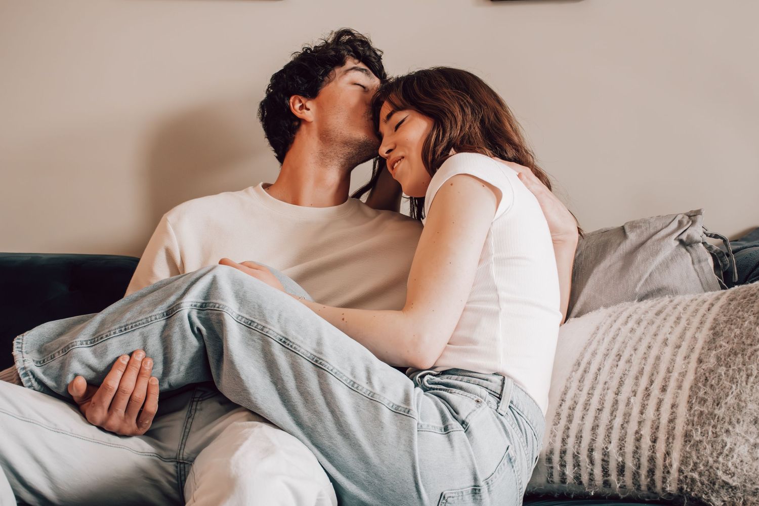 Romantic couple cuddling together on cozy grey couch at home while sharing intimate moments.