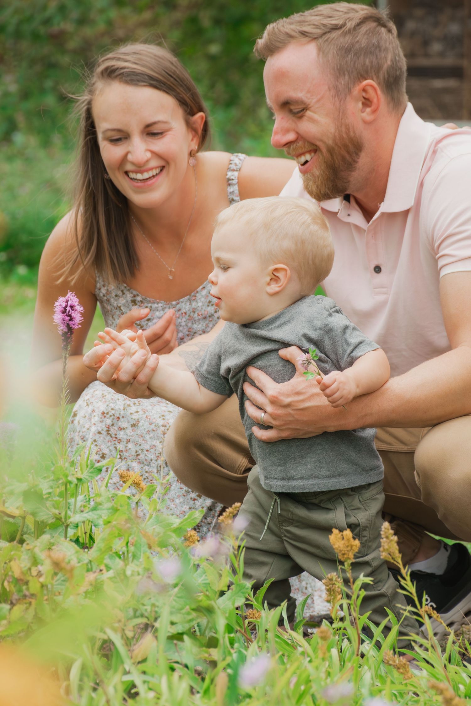 A family shares a joyful moment together while crouching among wildflowers in a garden setting.