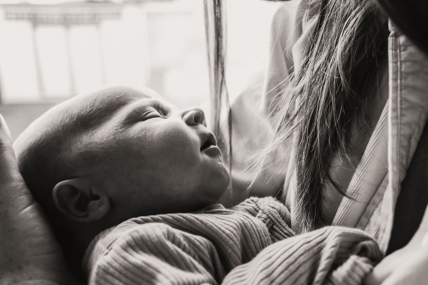 Black and white image of baby looking up while being held.