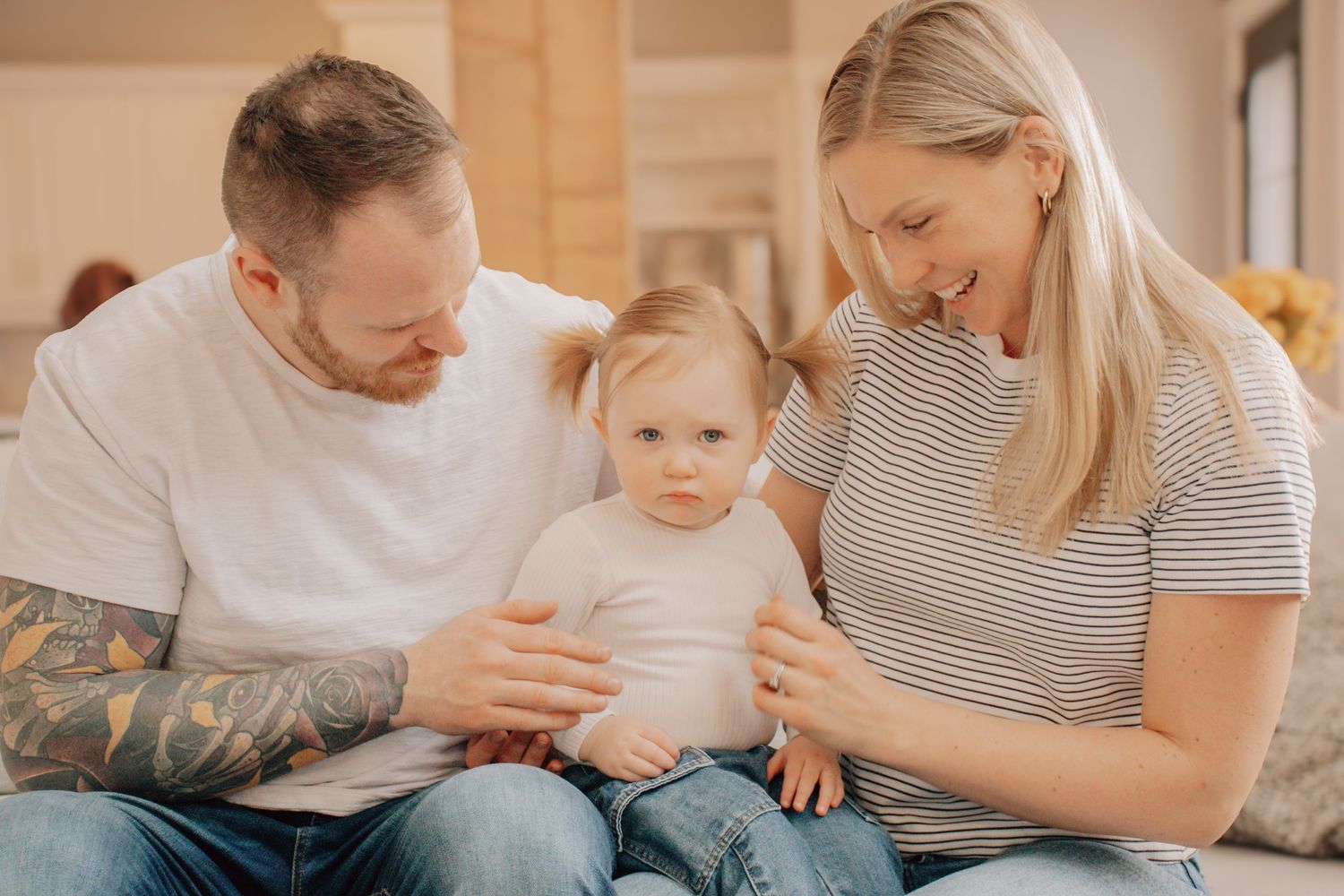 A happy family sits together on a couch sharing a tender moment in warm lighting.