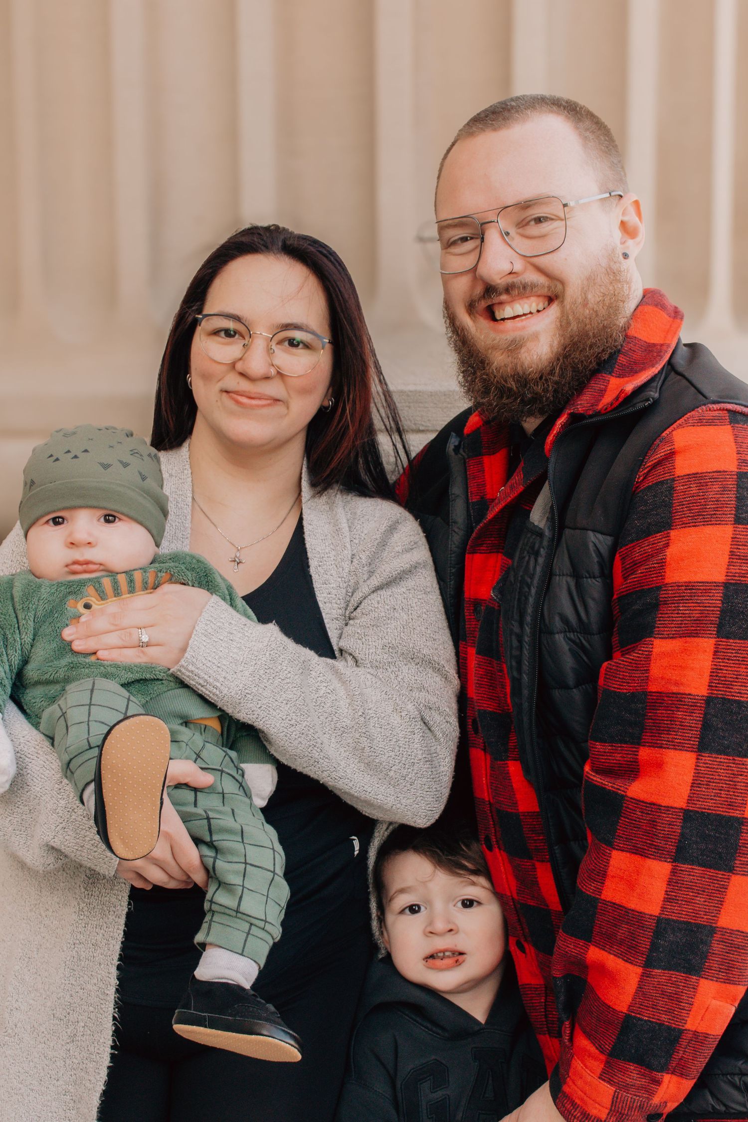 A family photo featuring two children, with one wearing green and one in black, against a beige background.