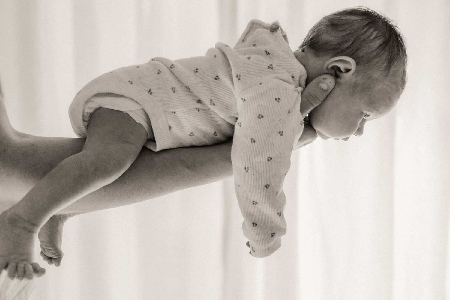Artistic black and white photo sequence showing a baby rolling over from left to right in four connected frames.