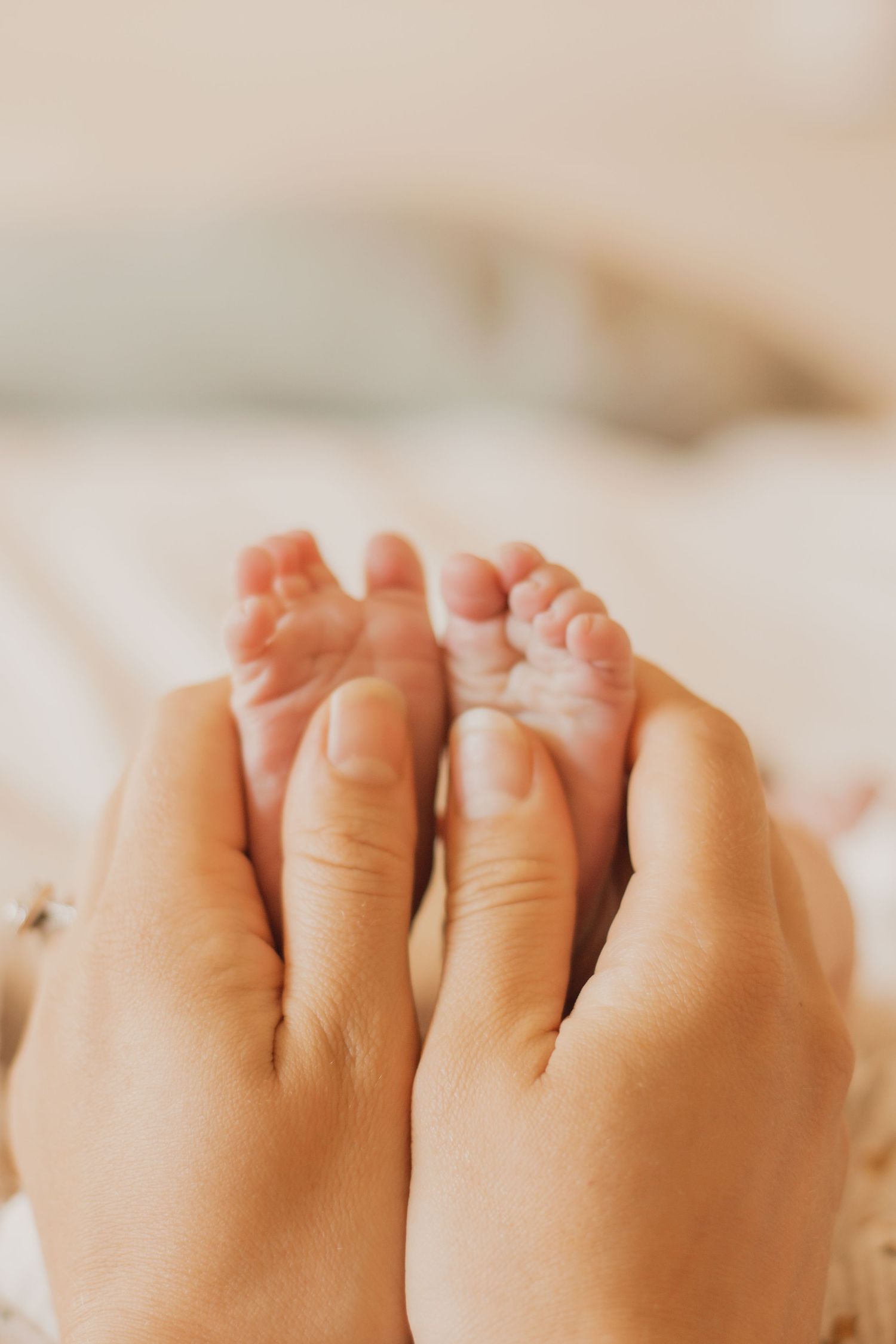 Tiny baby toes being gently held by adult hands against a soft white background.