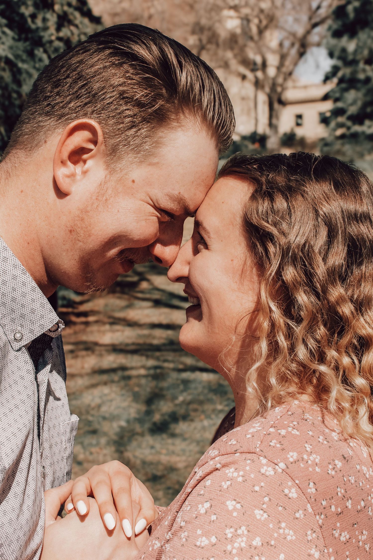Intimate romantic moment between couple outdoors with woman in pink floral dress and man in light shirt touching foreheads.