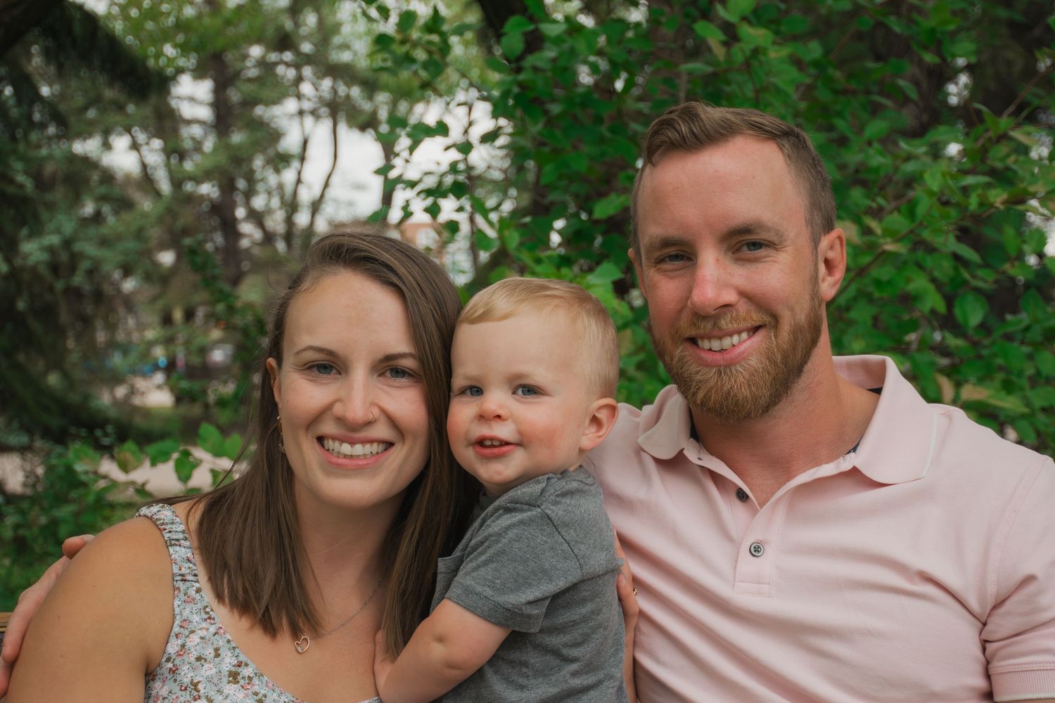 A family poses together outdoors with greenery in the background on a sunny day.