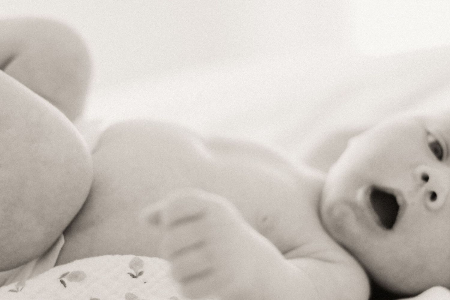Black and white photo series captures a baby's progressive movement across soft white bedding.