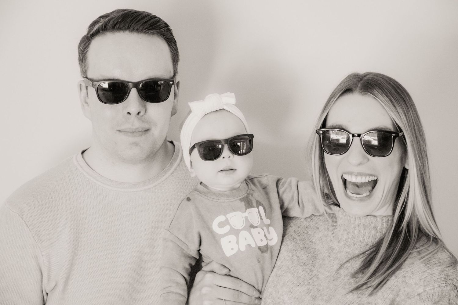 A stylish family wearing matching sunglasses poses for a black and white portrait.