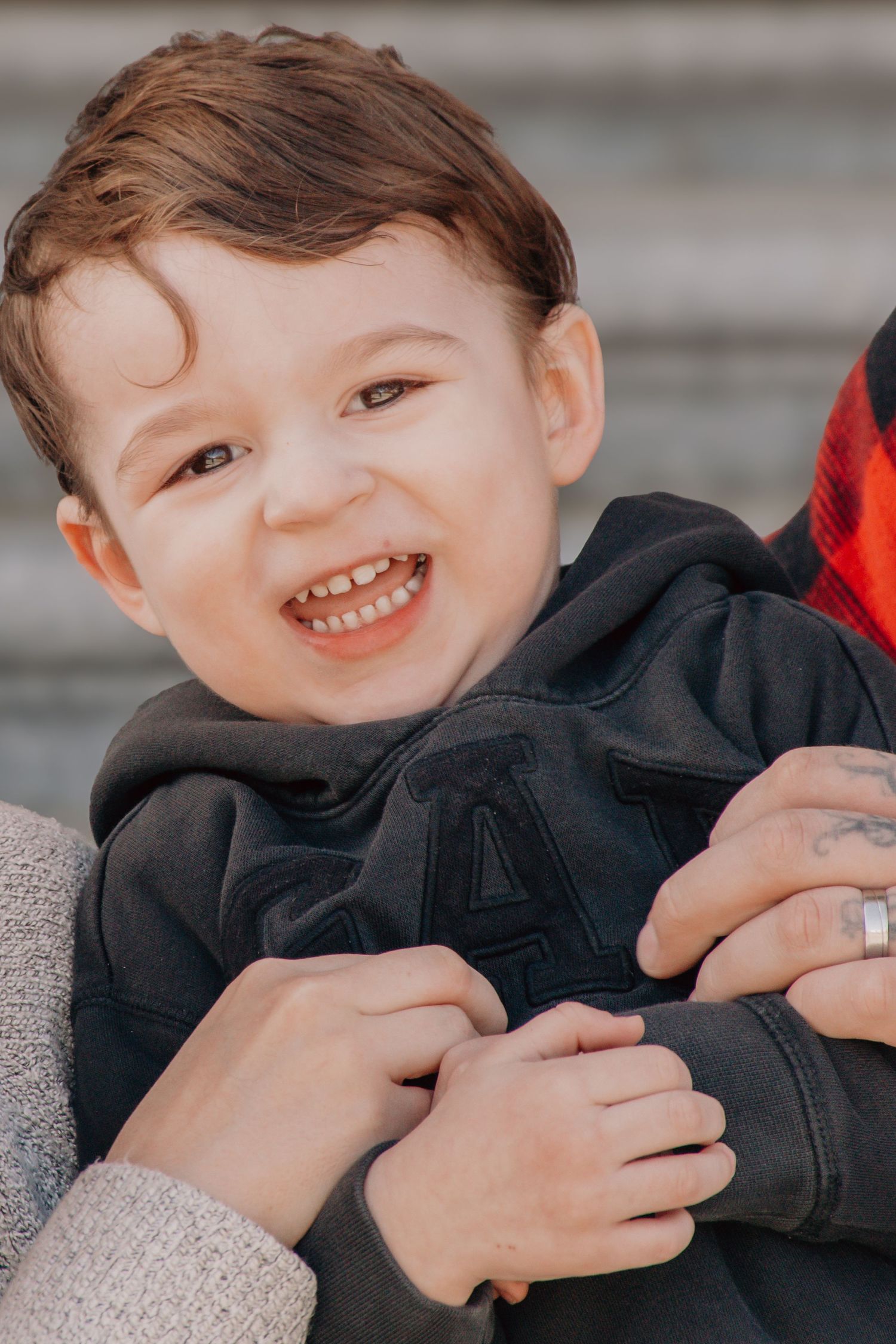 A joyful young child in a navy blue hoodie laughs while being embraced.