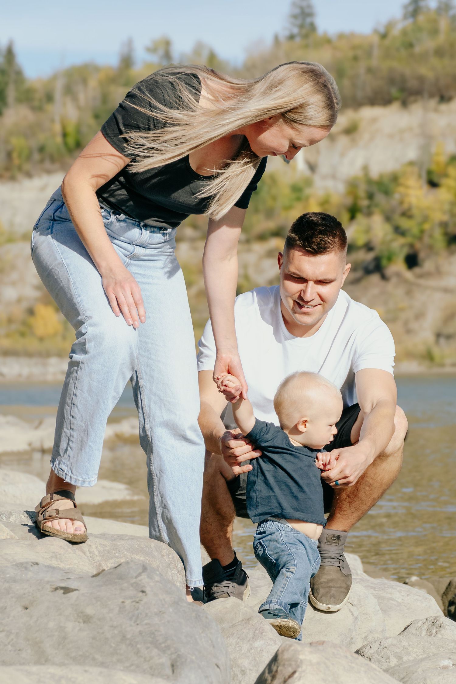 Family enjoying time together by a lake shore, exploring rocks and water on a sunny autumn day.
