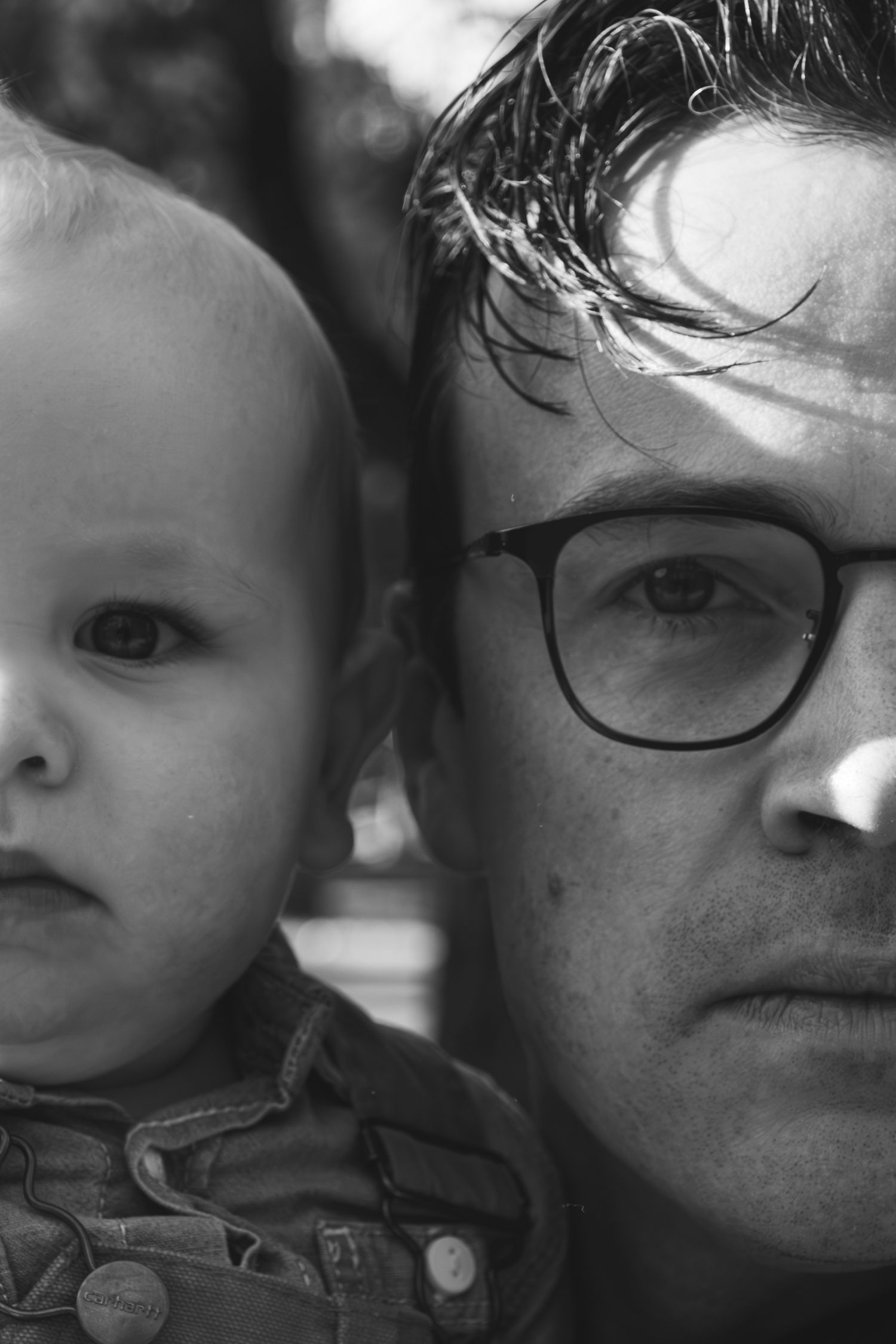A black and white close-up portrait of an adult wearing glasses and a small child together.