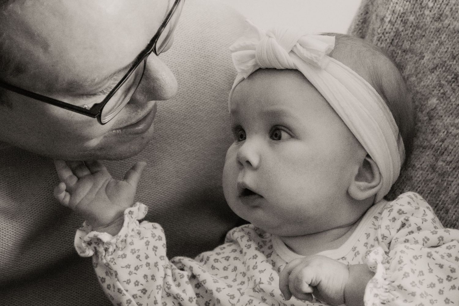 A tender black and white portrait shows a baby in white lace and a headband looking up with wonder.