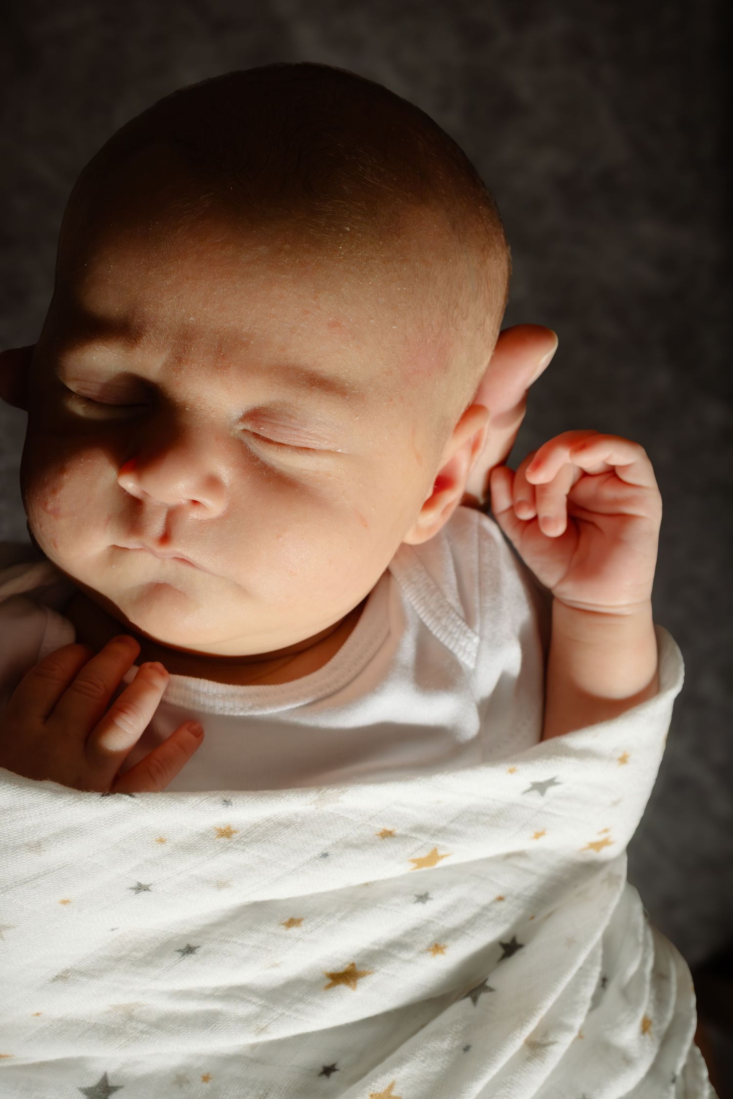 Close-up series of a sleeping baby's face against white bedding in dramatic lighting.