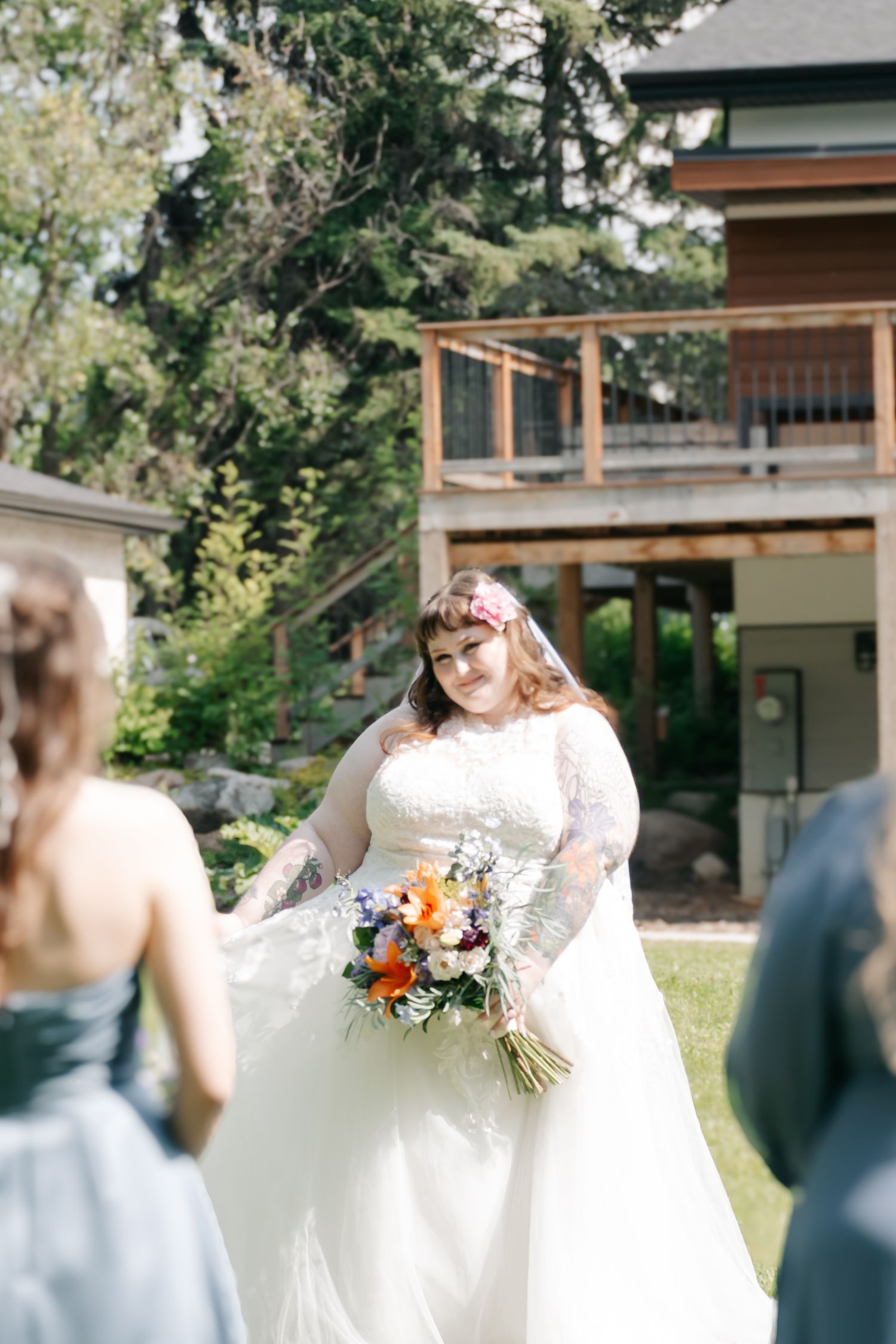 A long-sleeved lace wedding dress with a flowing white skirt and floral bouquet in an outdoor garden setting.
