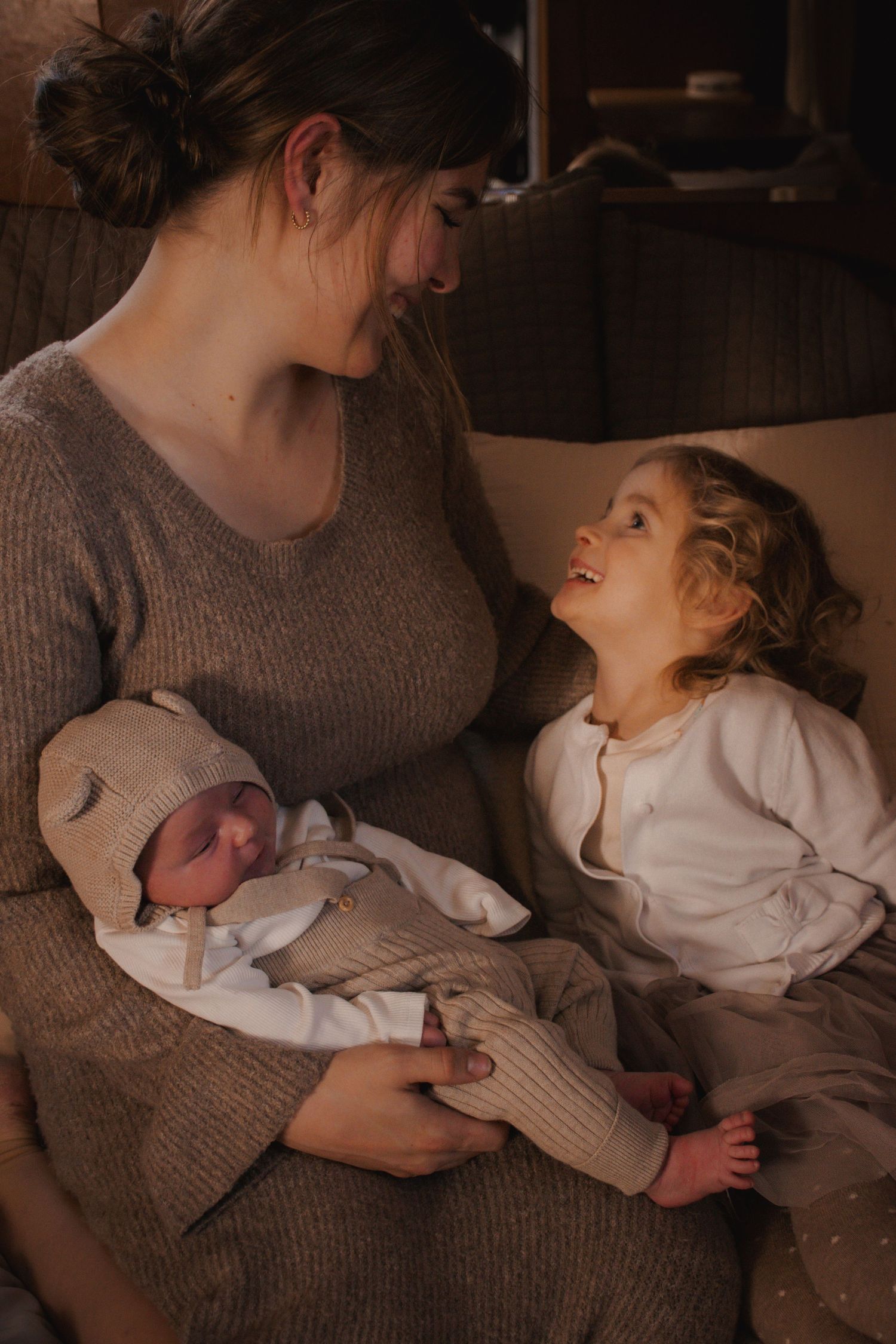 A warm intimate family moment as an older sibling looks adoringly at a newborn baby swaddled in neutral tones.