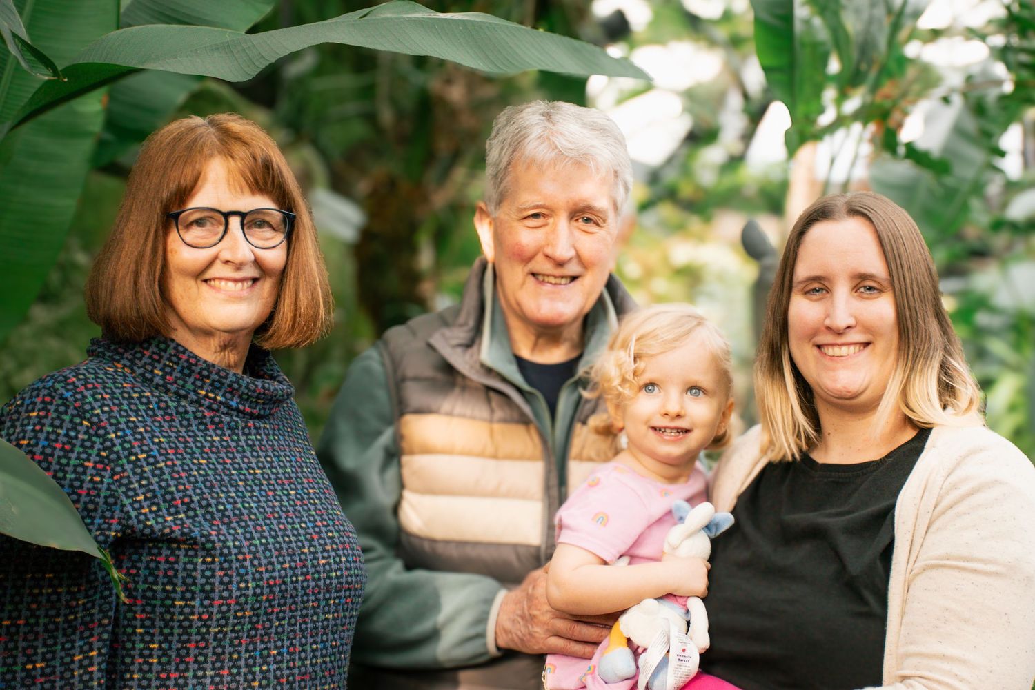 Multi-generation family portrait with four people in casual attire standing together indoors.