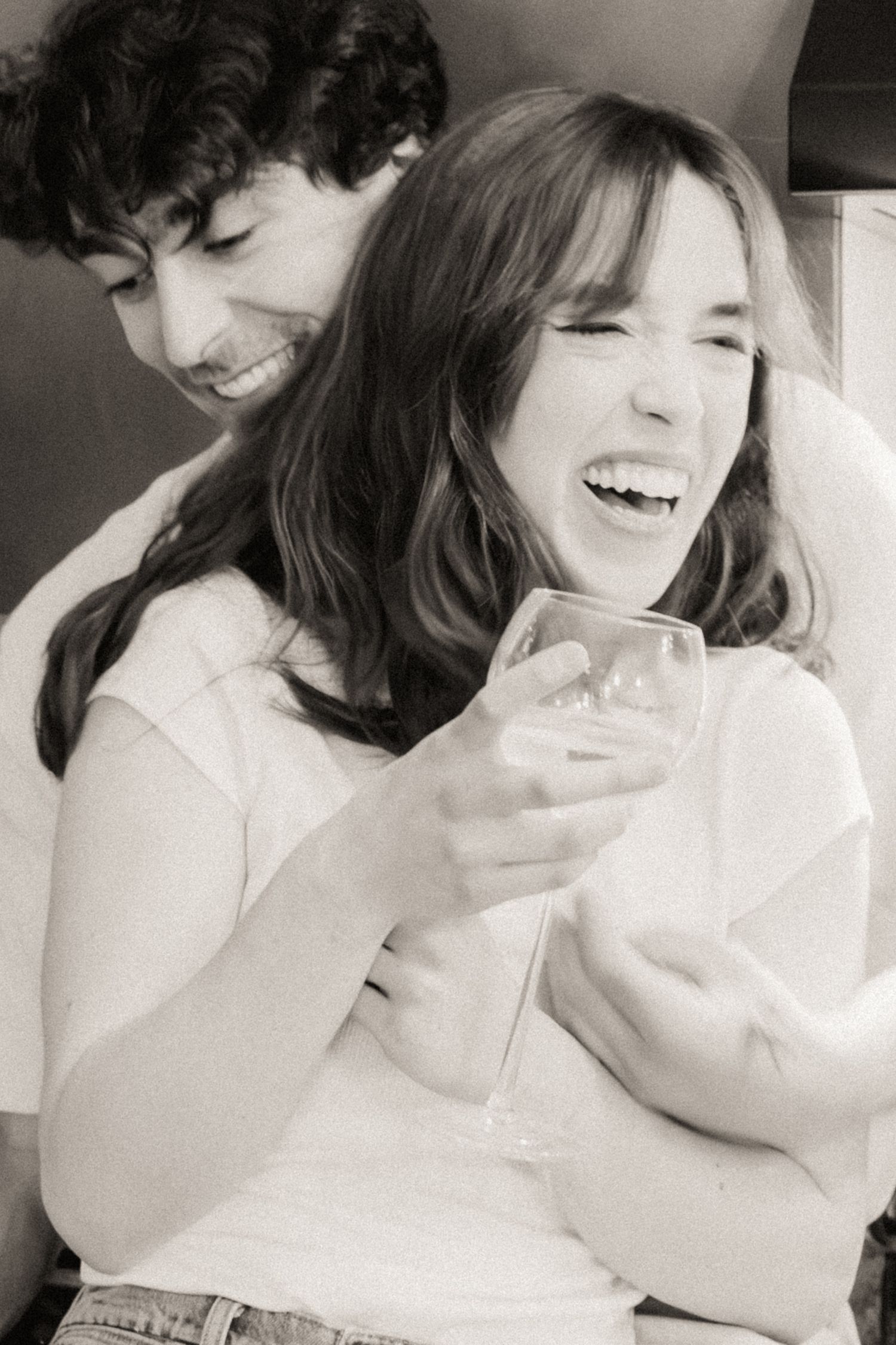 A joyful candid black and white moment showing two people laughing together while one holds a wine glass.