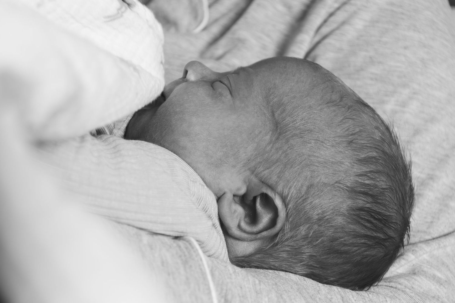 A series of black and white photographs showing a baby sleeping peacefully on white bedding.