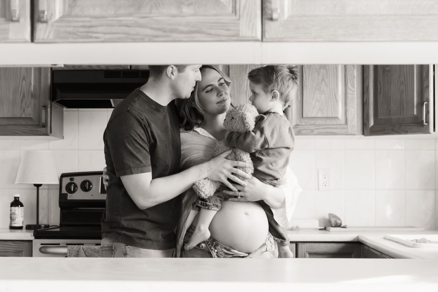 A black and white photo of a family moment in their kitchen, with parents and child gathered together.