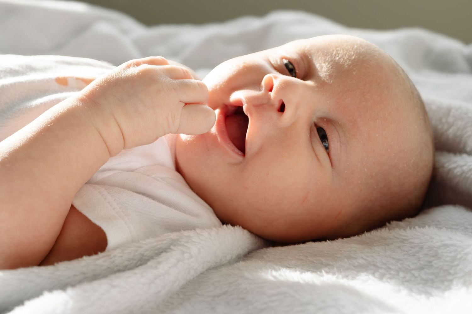 A baby lies on soft white bedding while looking to the side with a peaceful expression.