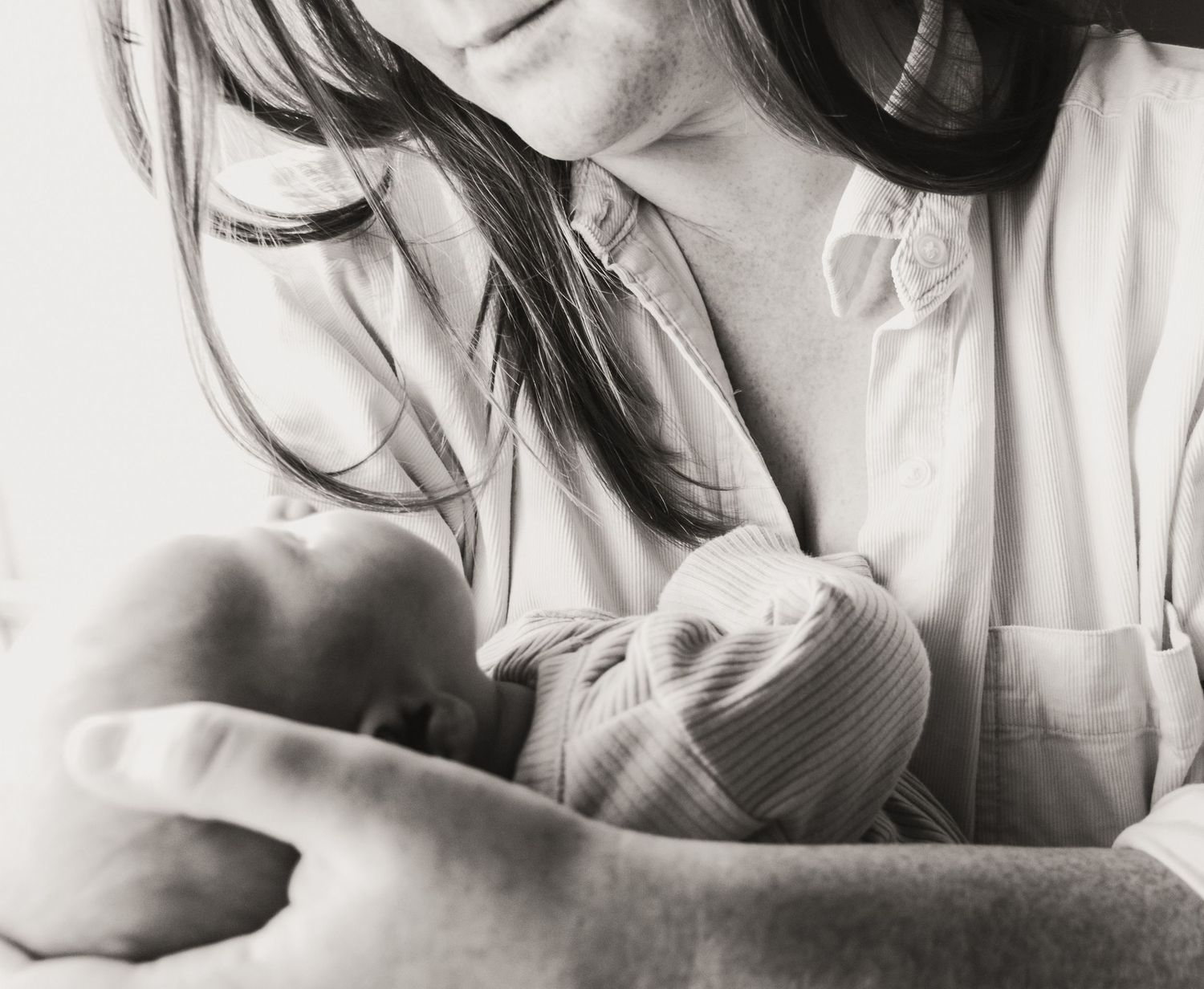 A tender black and white photograph showing a newborn baby being cradled in a striped blanket.