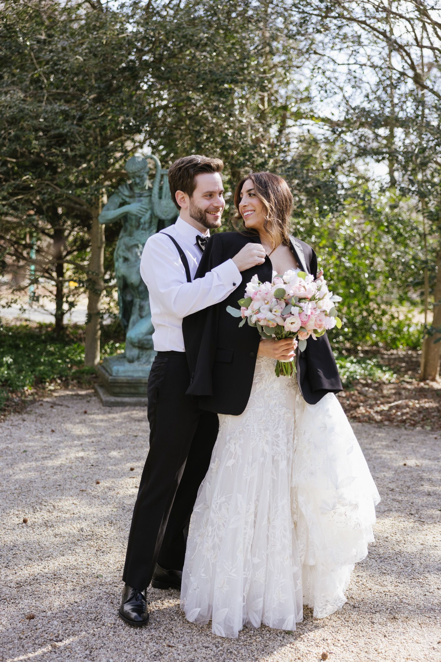 Groom placing his jacket over bride's shoulders at a park in NY