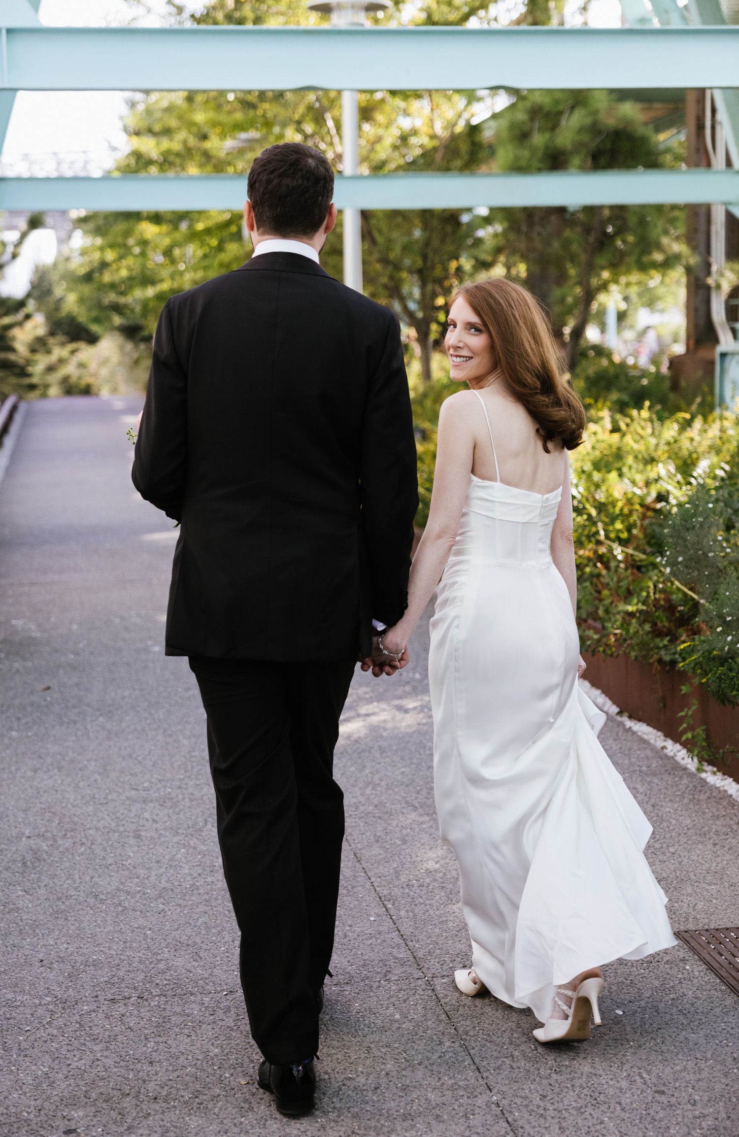 Couple holding hands as bride looks over shoulder at Domino Park in Brookyn New York