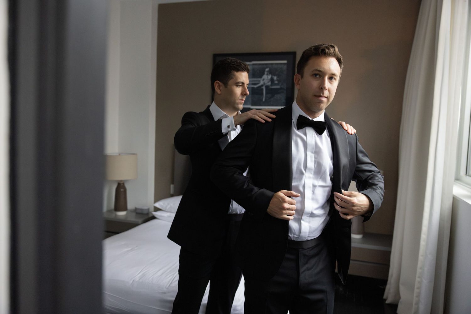 Friend helping groom put jacket on before his wedding in NYC