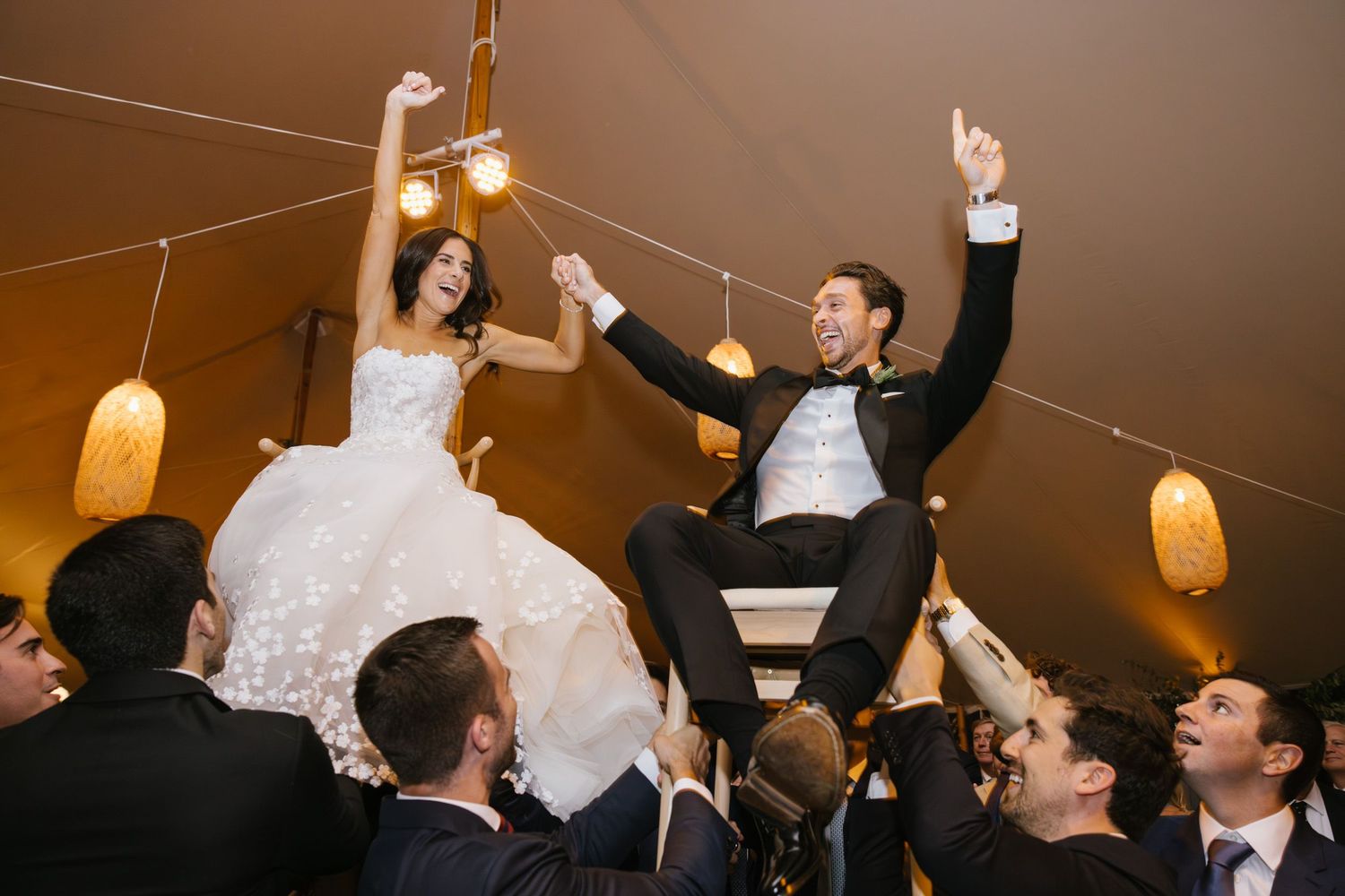 Bride and groom lifted in chairs during joyful Jewish wedding hora dance celebration inside elegant tent reception in NY