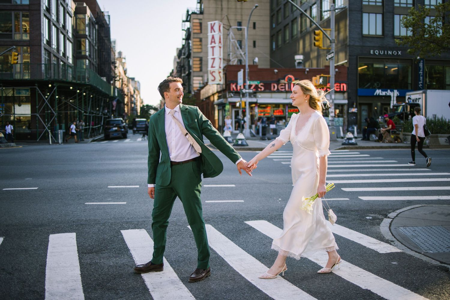 Couple holding hands crossing a street in New York City with Katz's Deli in background.