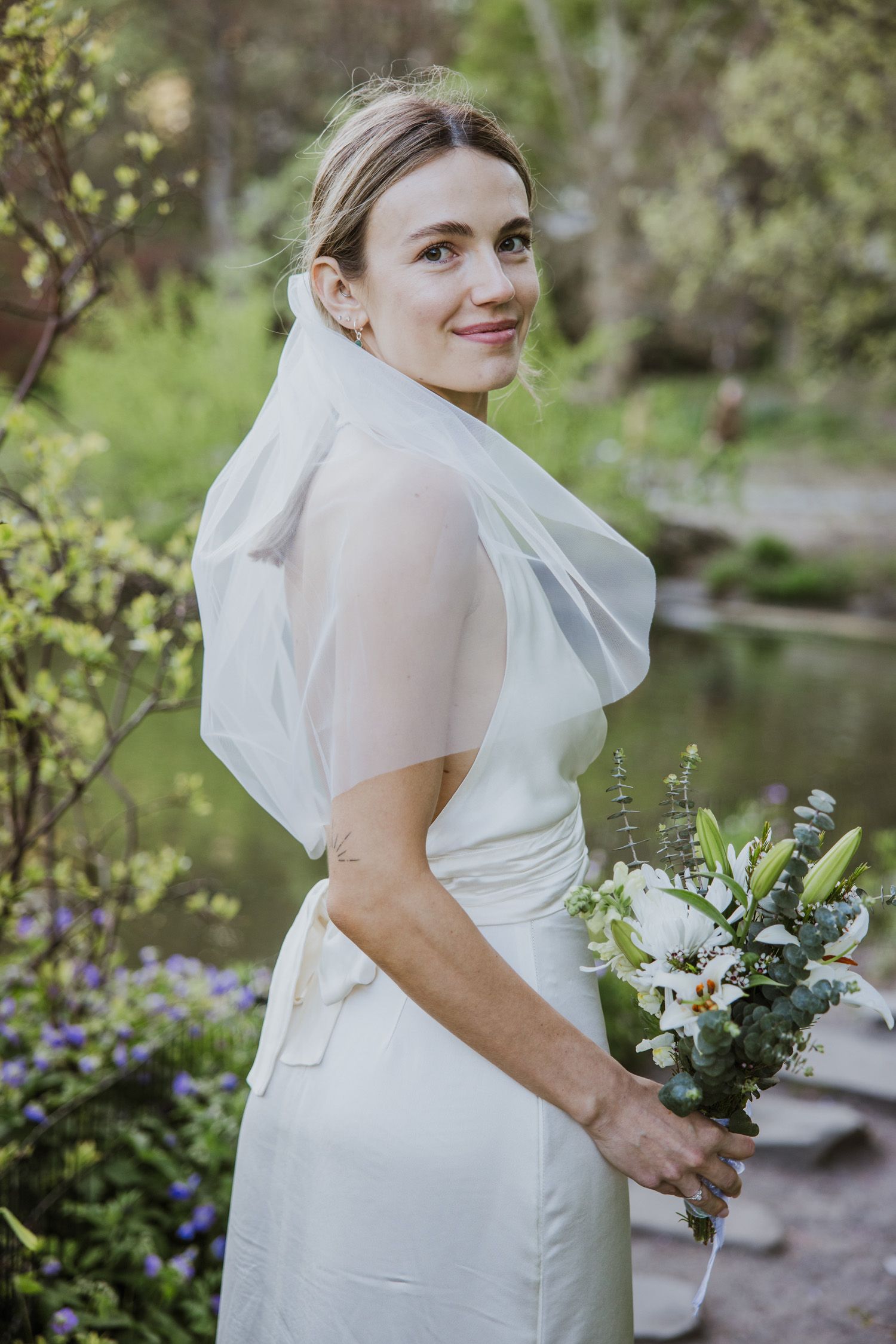 Bride in white gown and veil holding white lily bouquet before her wedding in Central Park in NYC