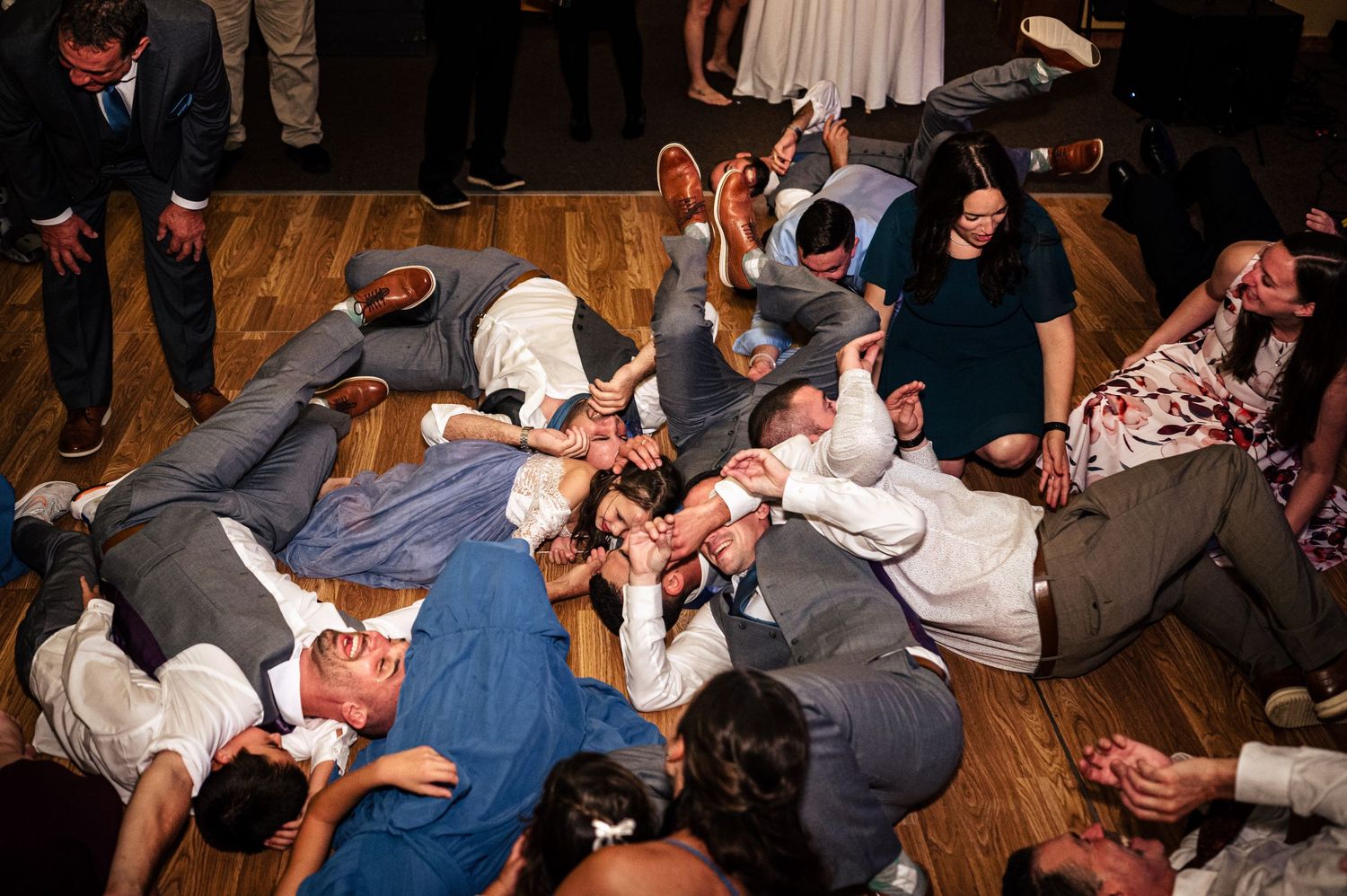 Wedding guests lying on dance floor in a playful group pile during lively reception celebration.