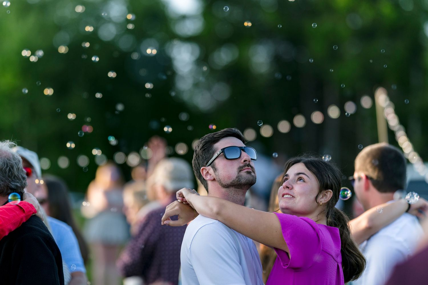 Couple dancing outdoors at a festive evening event with string lights and bubbles floating in the air.