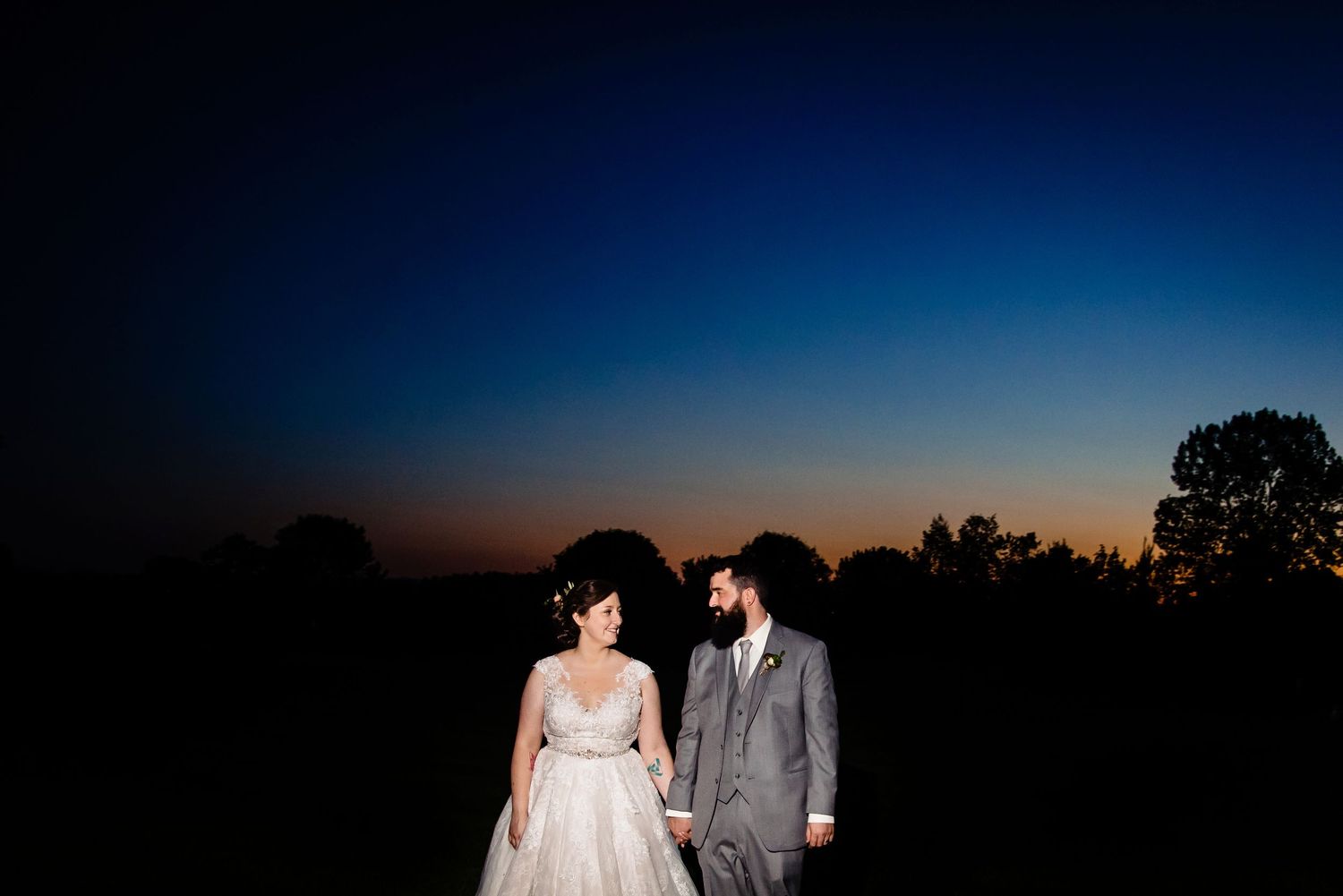 Bride and groom silhouetted against a stunning twilight sky at sunset during their outdoor wedding celebration.