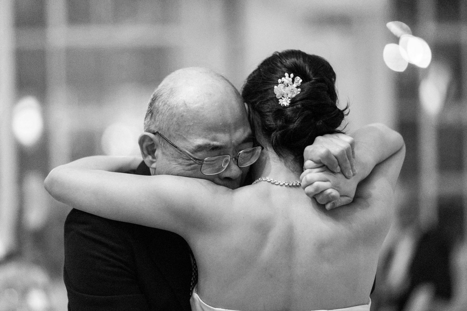 Black and white photo of a bride and elderly man sharing an emotional dance embrace at a wedding reception.