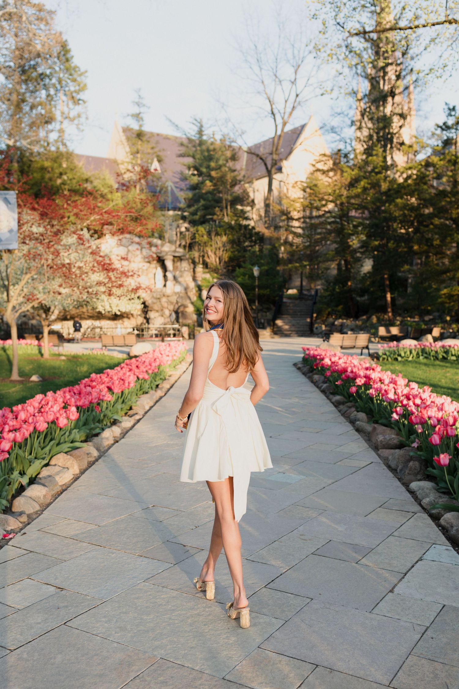 A white sundress and spring tulips line a stone path through a garden on a sunny afternoon.