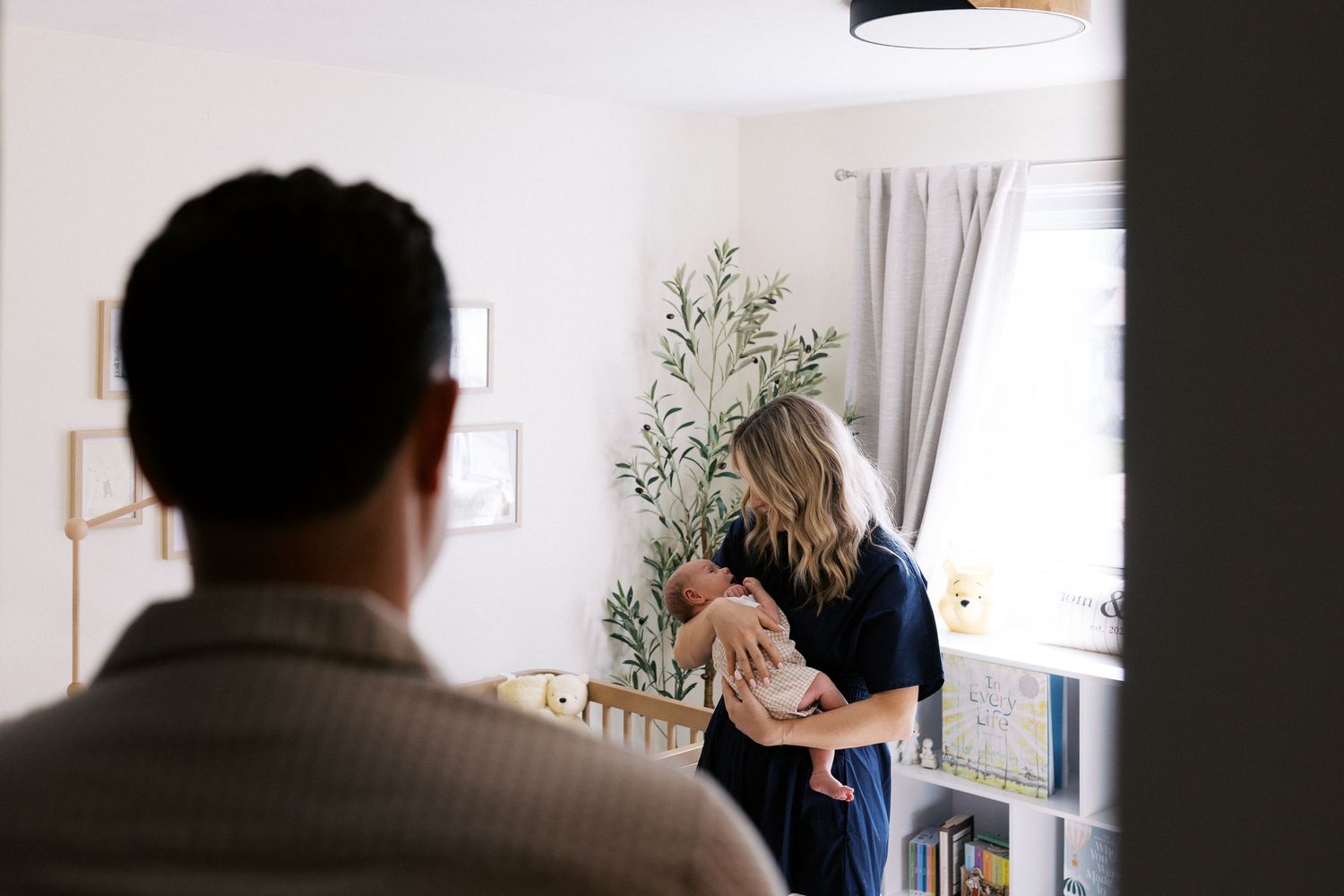 A candid indoor scene showing people gathered near white curtains and a decorative plant at home.
