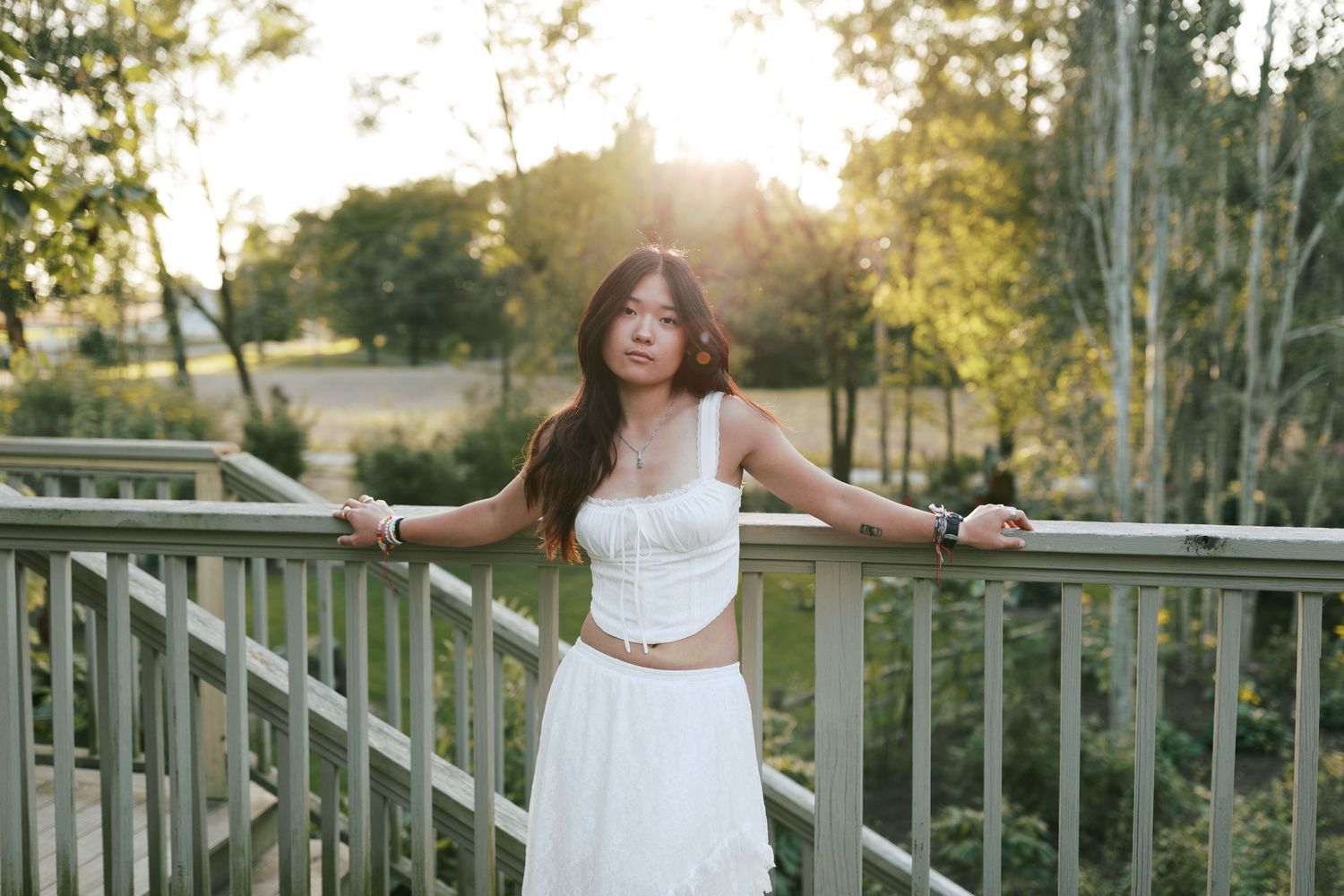 A woman in a white dress poses gracefully on a wooden bridge during golden hour sunset.