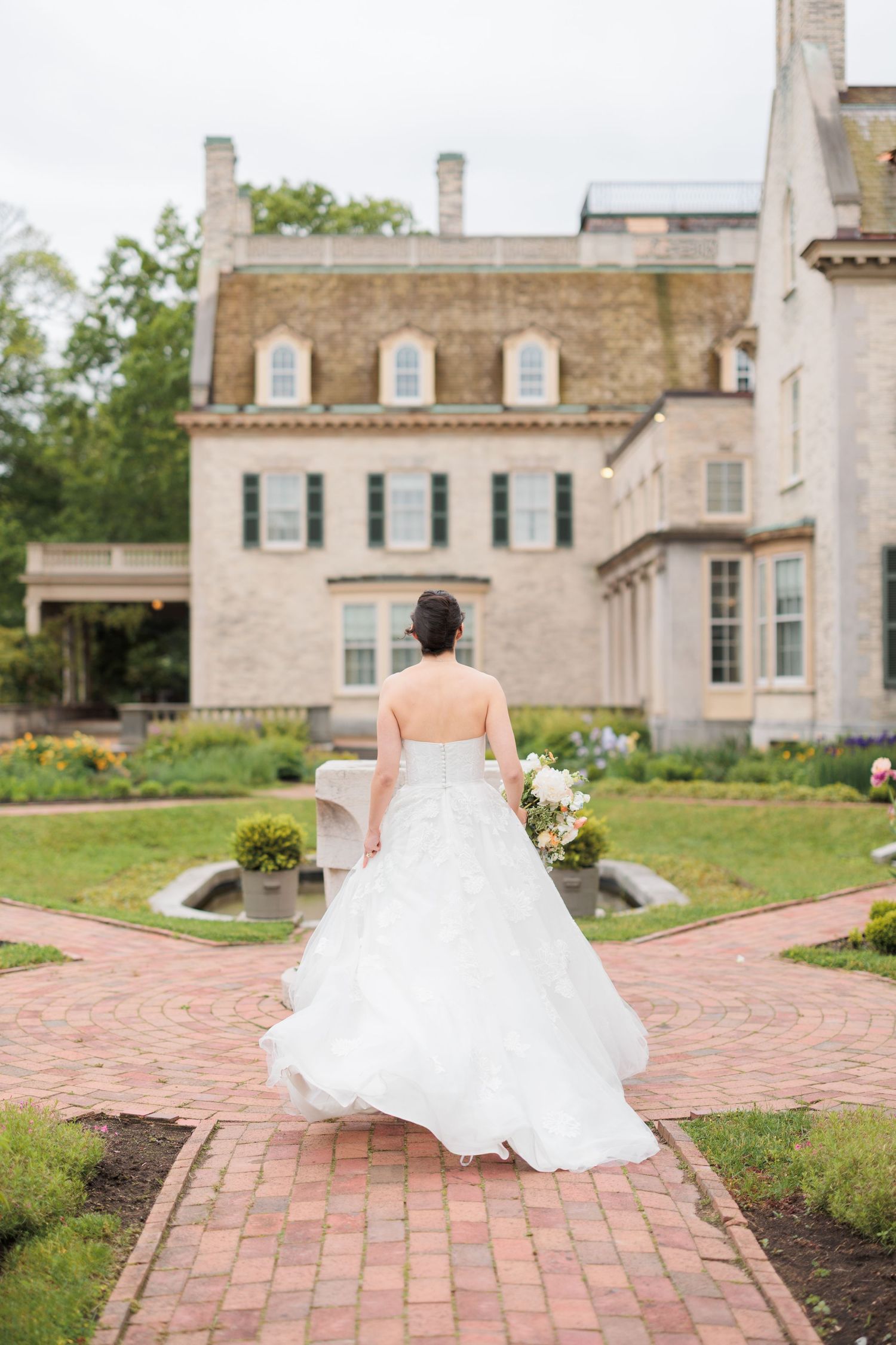 Bride in flowing white dress poses in front of elegant stone mansion with brick pathways.

Rochester NY wedding photographer