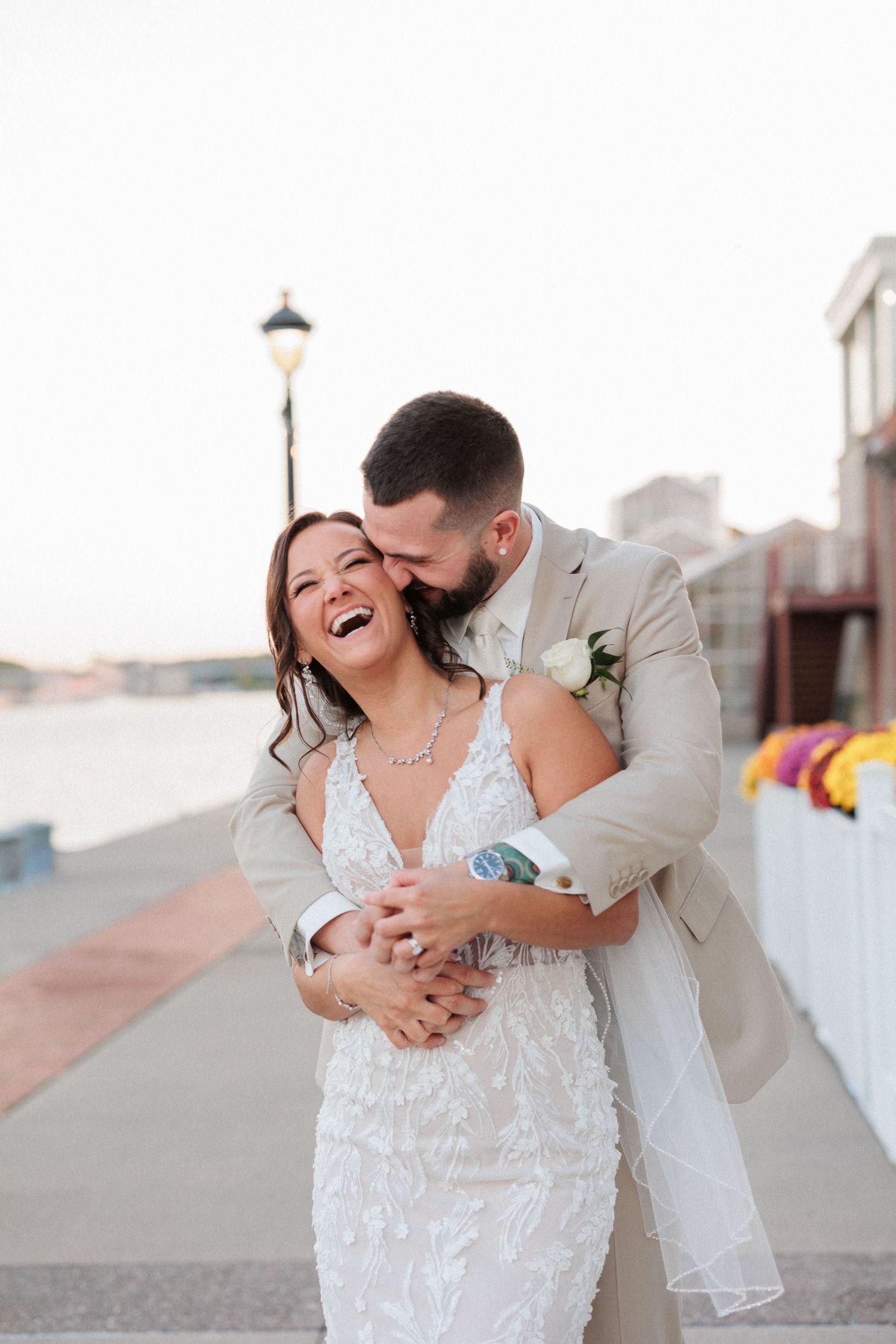 A joyful wedding couple shares a romantic moment on a boardwalk during sunset.