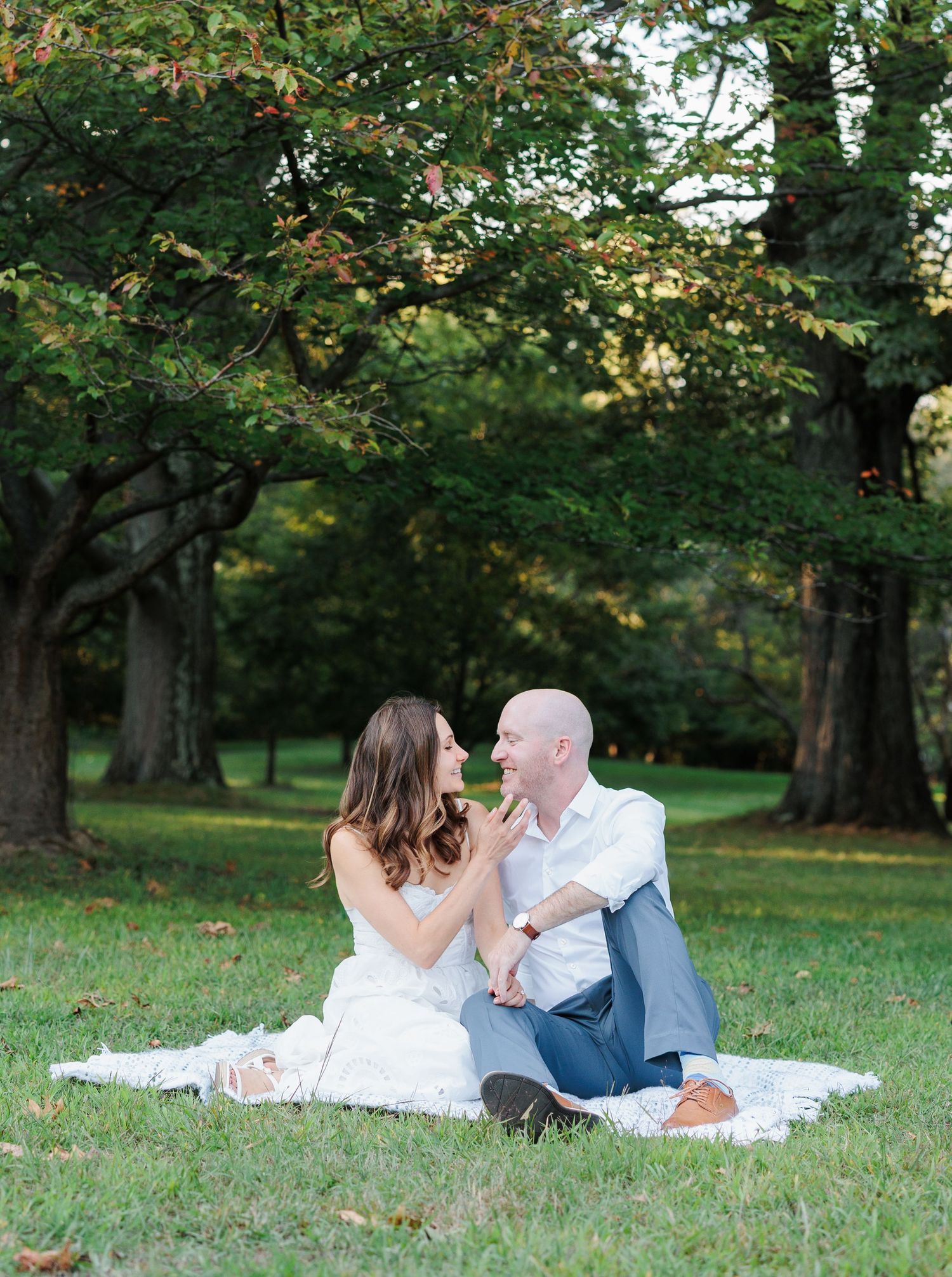 A couple sharing an intimate moment while sitting on a blanket in a lush green park.
