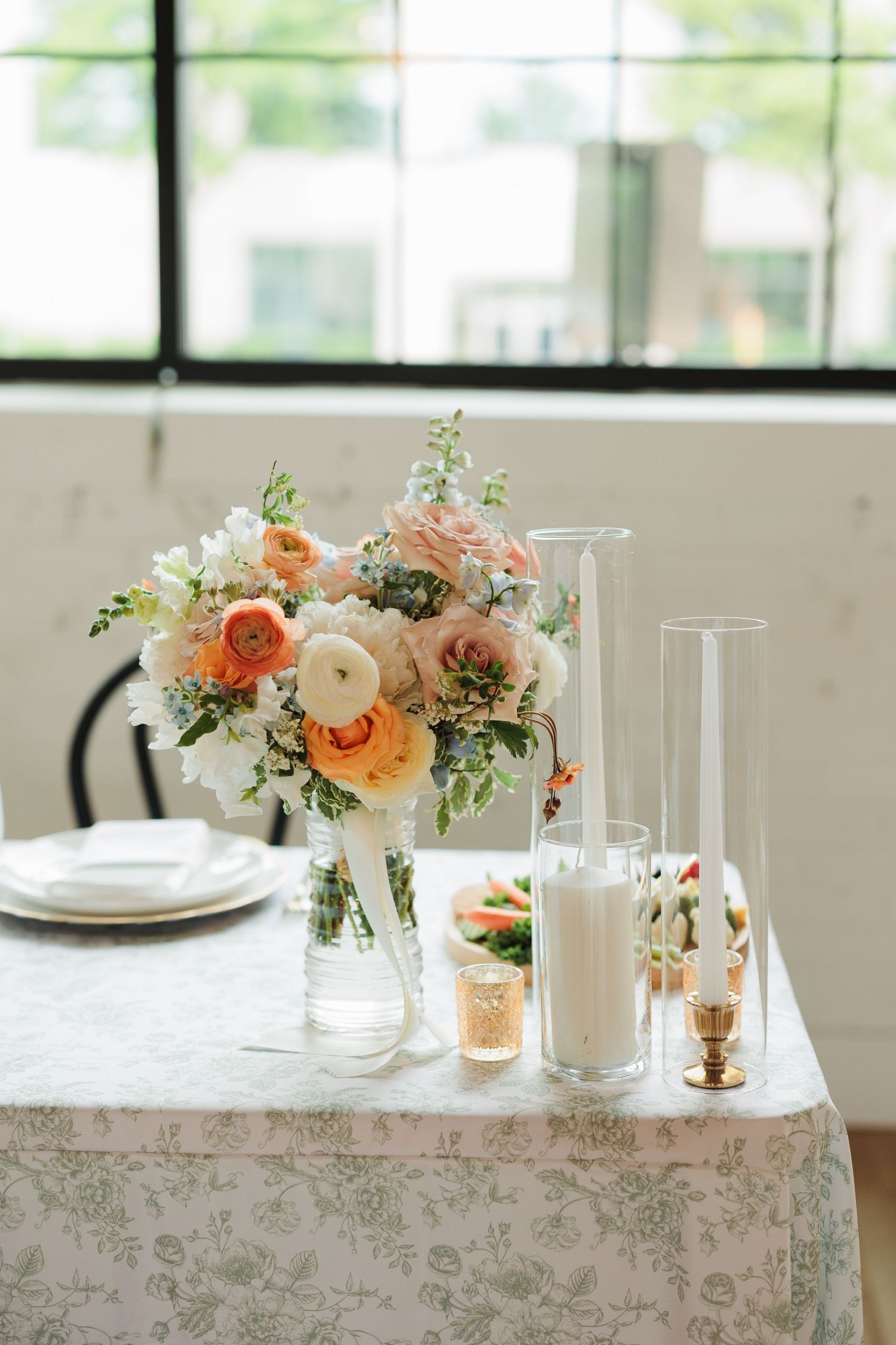 A romantic table setting with peach floral centerpieces and glass candleholders.