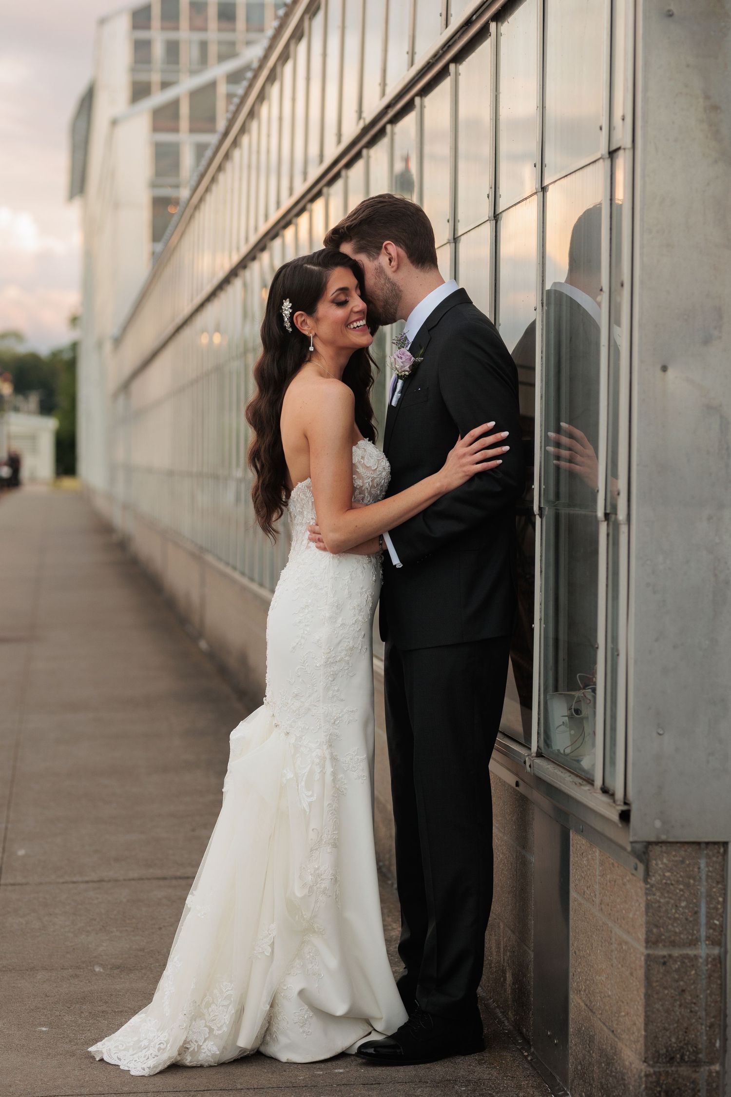 A romantic wedding couple embracing against a concrete wall during an outdoor photo session.