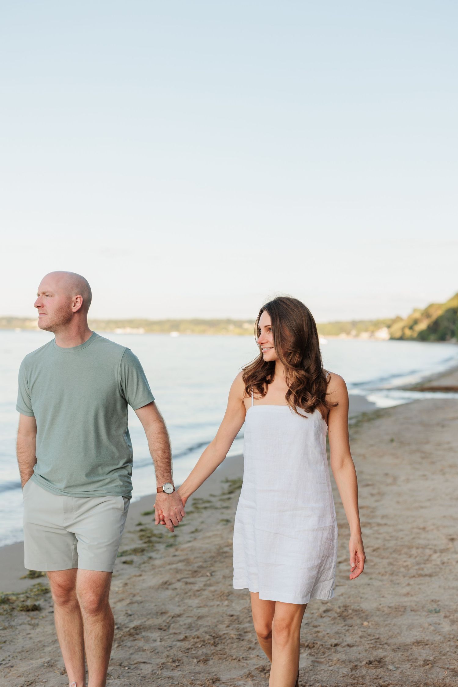 A couple walking hand in hand along a peaceful beach during golden hour.